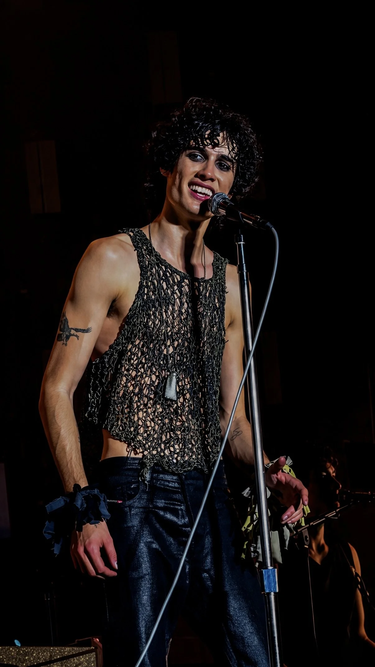 Sombr smiling at the microphone during a live concert.
