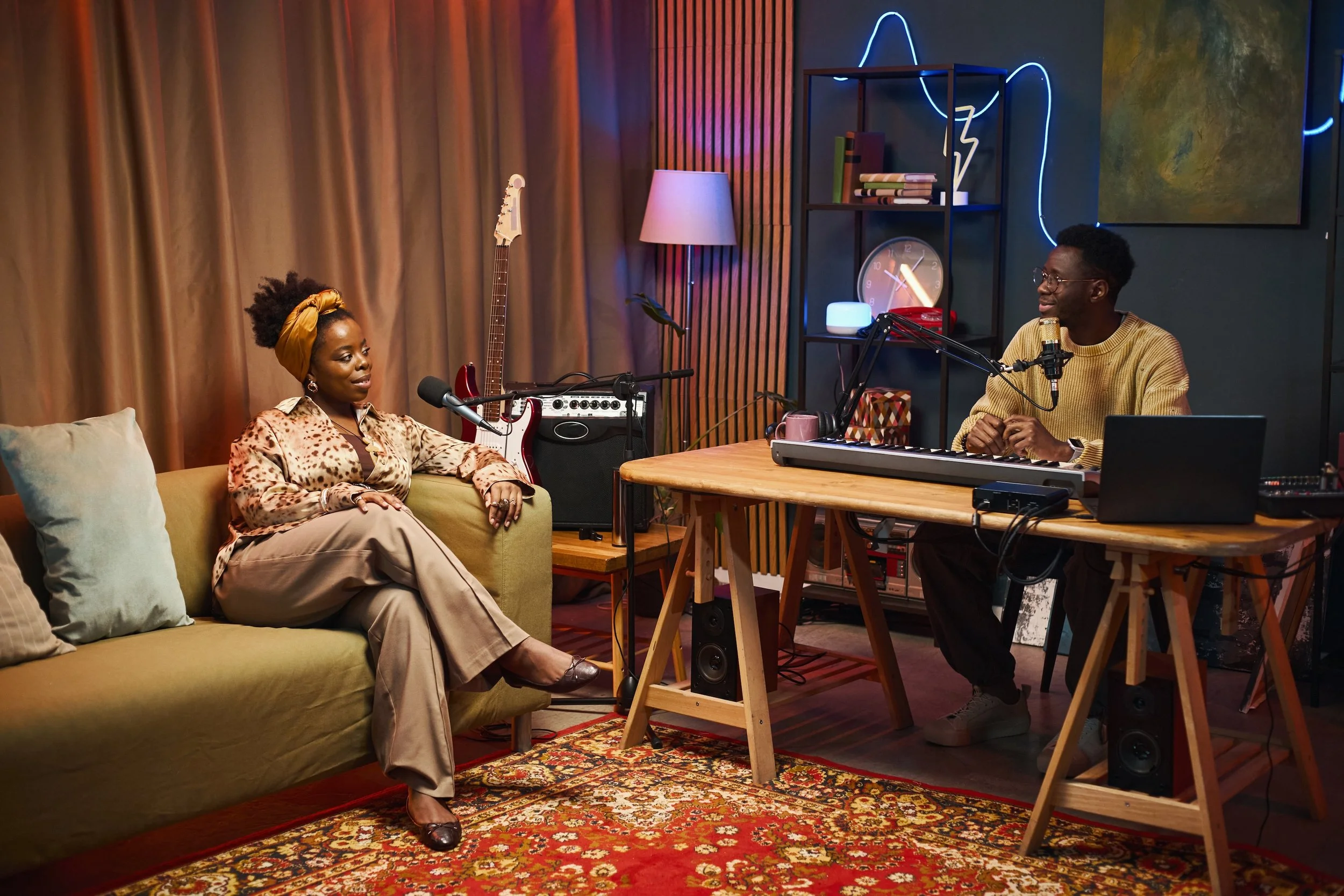 Two people having a conversation in a cozy, modern room with musical equipment, books, and decorative lighting.