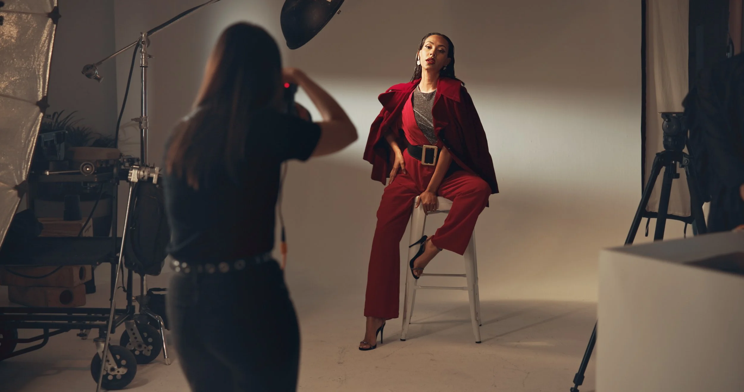 A woman in a red suit and black high heels posing in a photography studio
