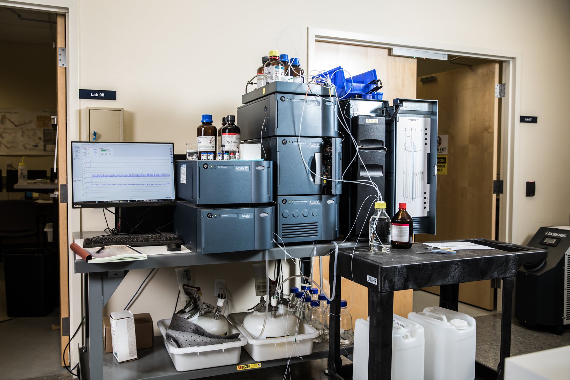 Laboratory setup with scientific equipment, bottles, and a computer monitor displaying data.