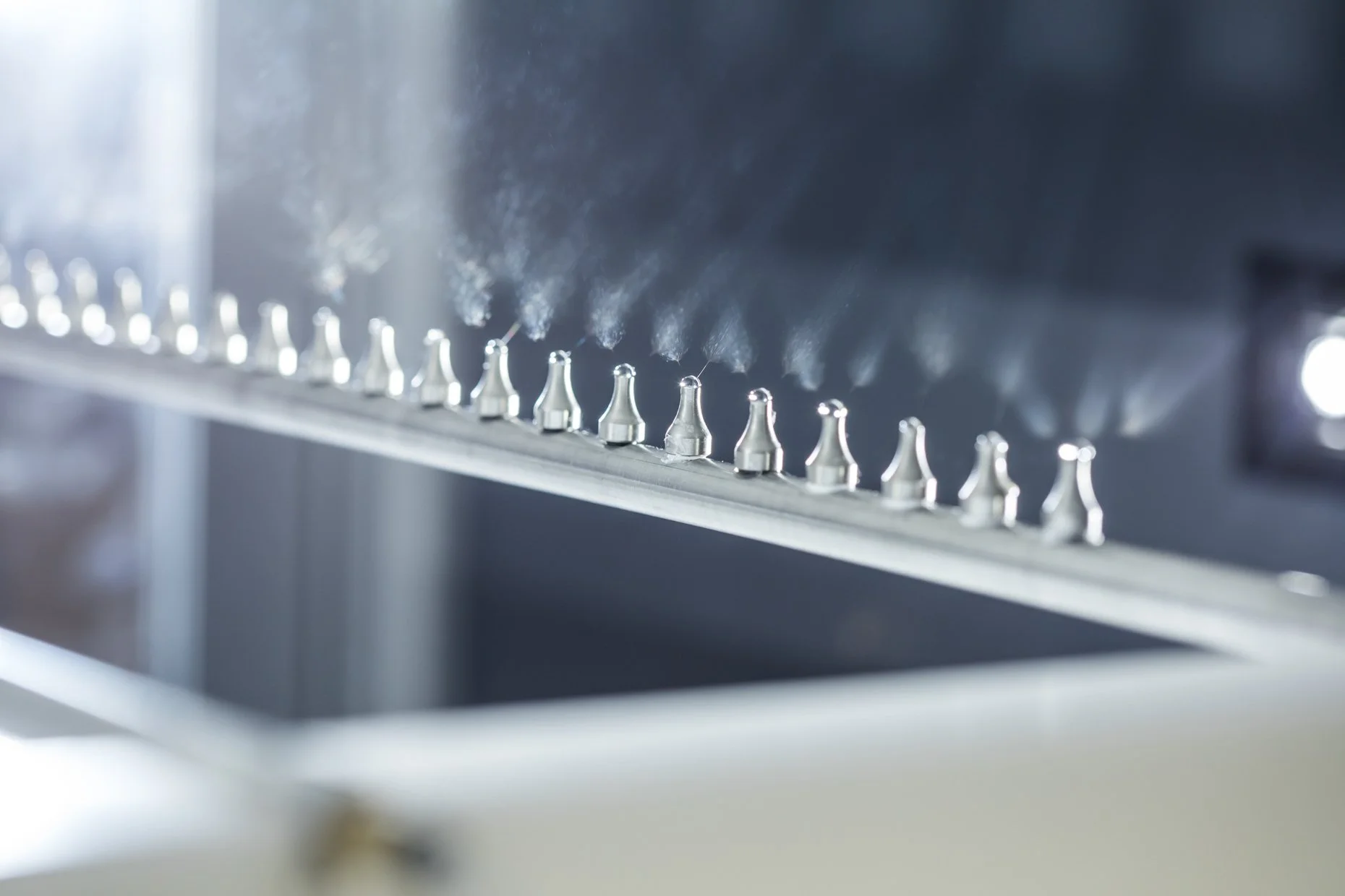 Close-up of a metal conveyor belt with small, cone-shaped objects on it, emitting smoke or vapor.