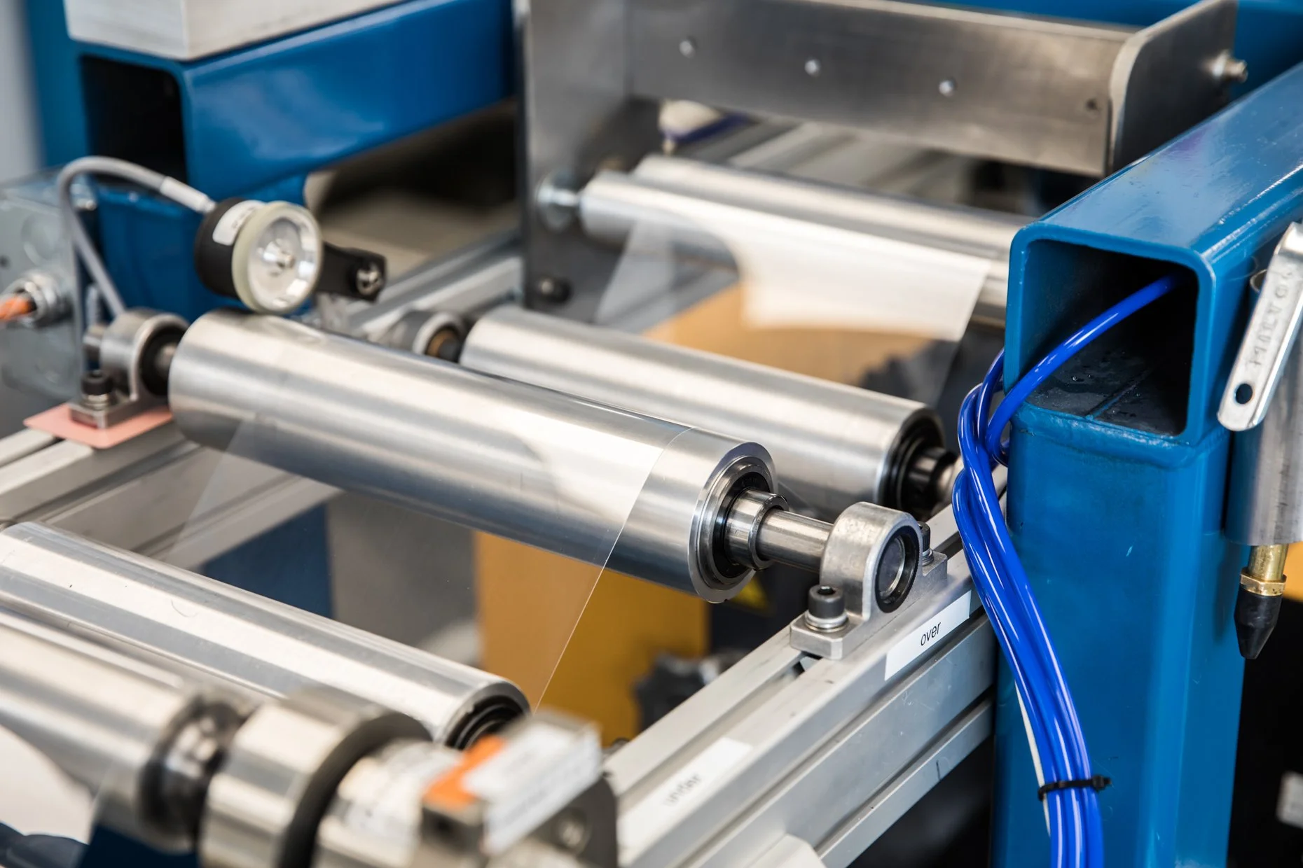 Industrial machine with metal rollers and a blue housing, possibly in a manufacturing or packaging facility.