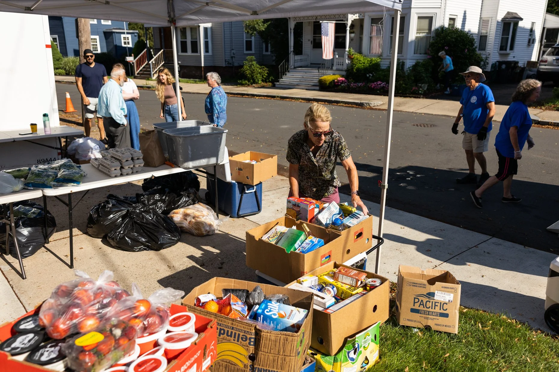 People recycling and distributing donated food and supplies under a canopy on a residential street.