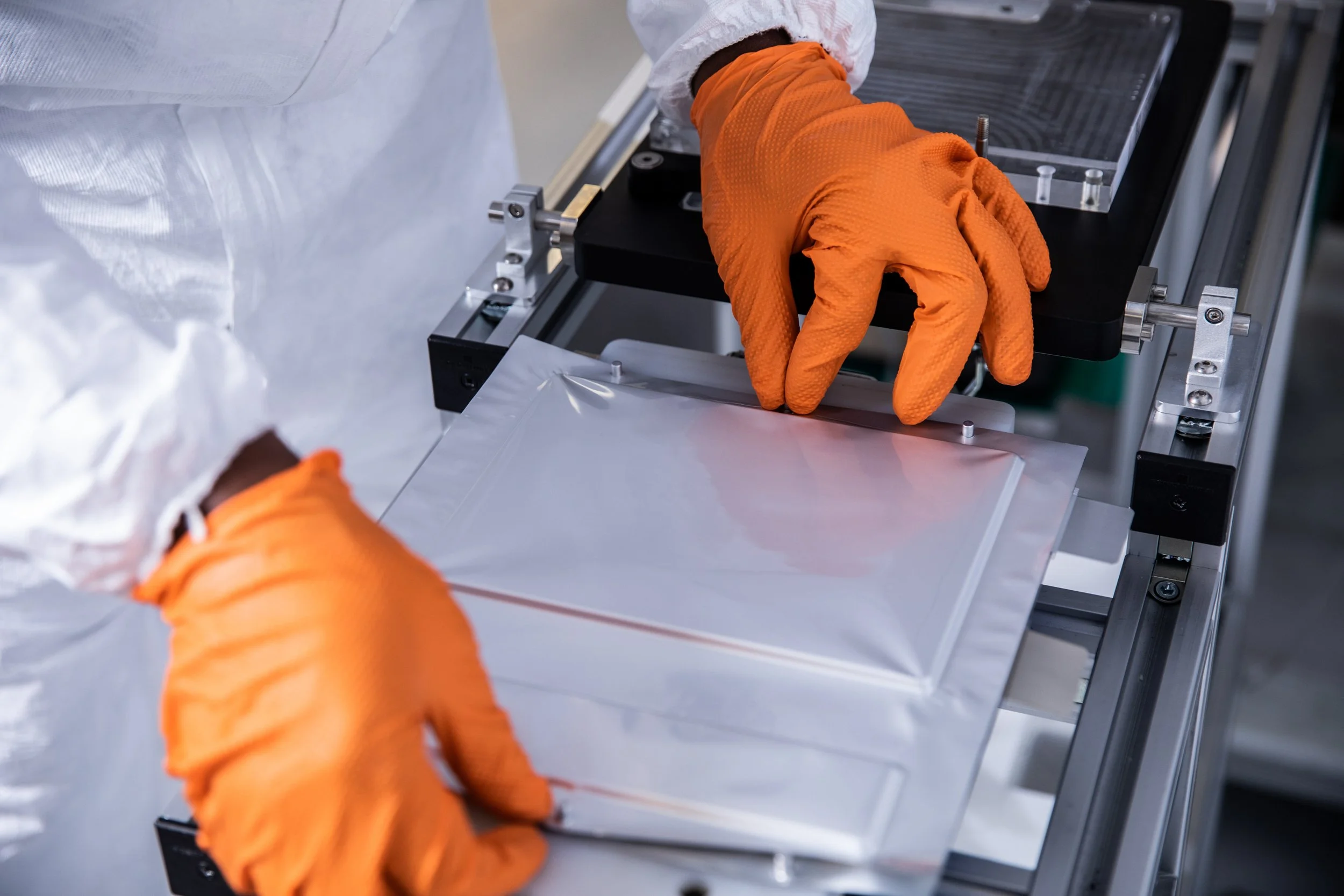 Hands wearing orange gloves working with a scientific or laboratory equipment in a clean environment.