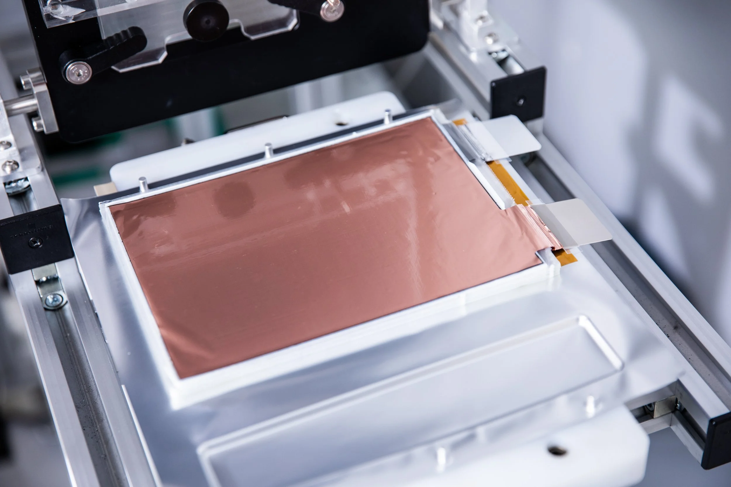 Close-up of a scientific or industrial machine with a copper-colored component and various metallic and plastic parts.