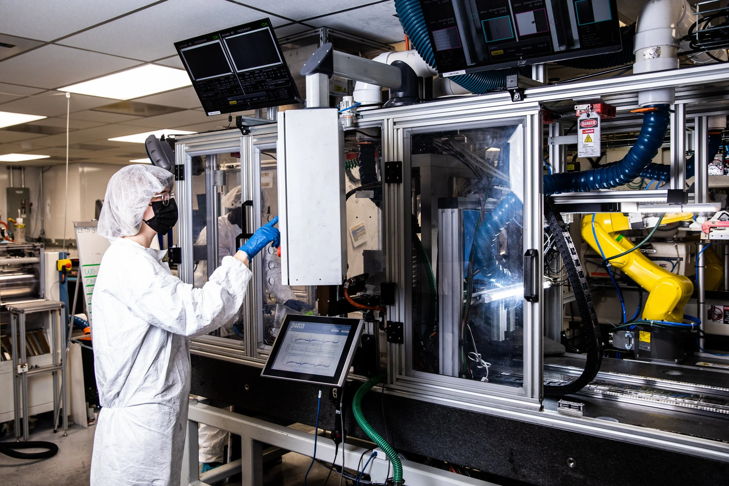 Scientists in protective gear working on a large industrial machine in a laboratory or manufacturing facility.