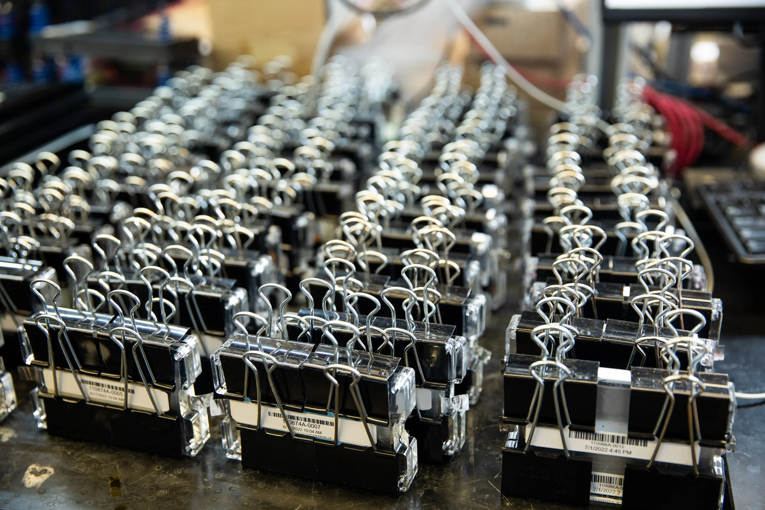 A row of black binder clips with silver metal handles, stored on a black surface.