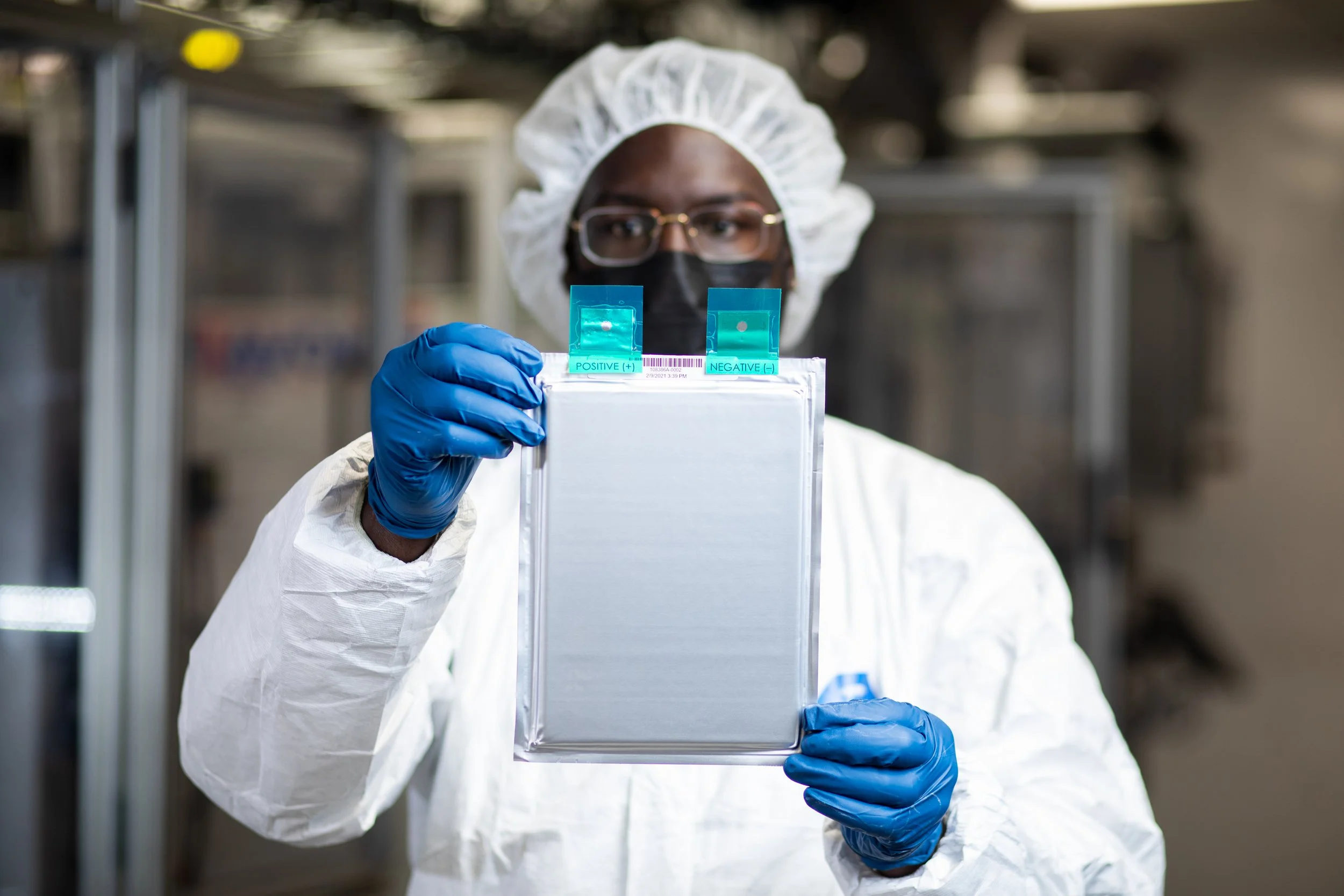 A scientist in protective gear holding a transparent card indicating a positive COVID-19 test result.