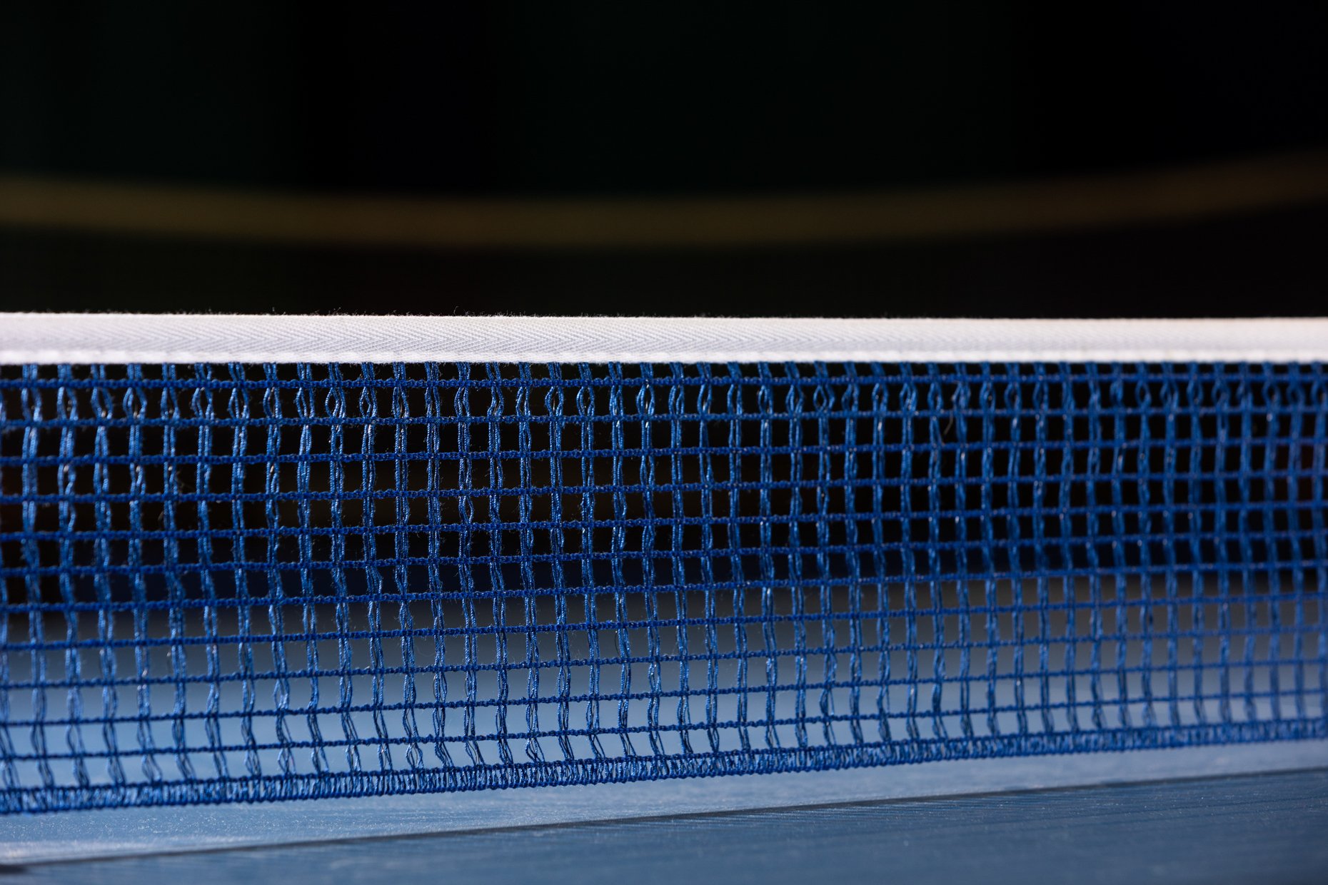 Close-up of a blue and white tennis net with a dark background.