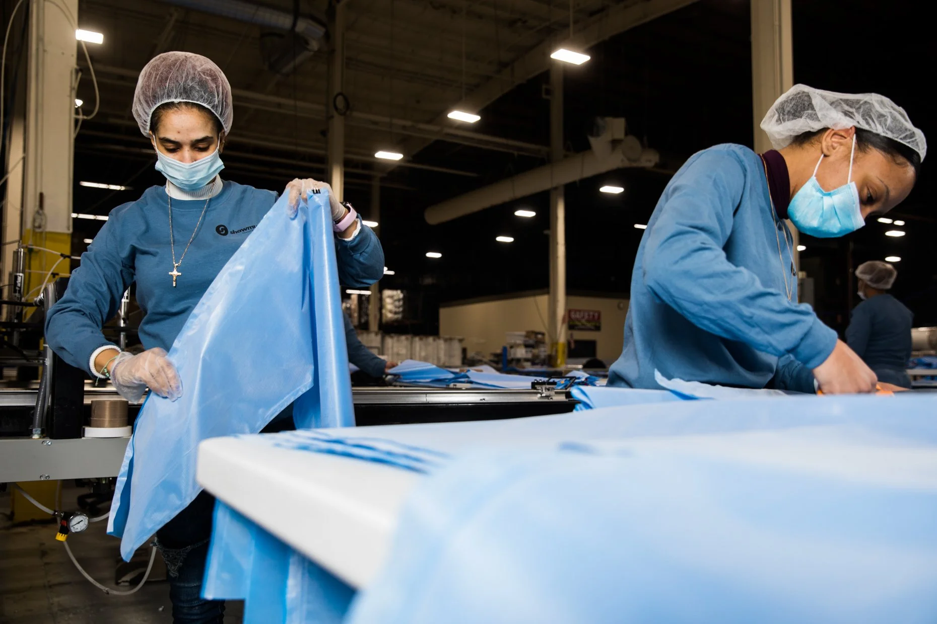 Workers in blue uniforms, hairnets, and face masks working with fabric in an industrial factory setting.