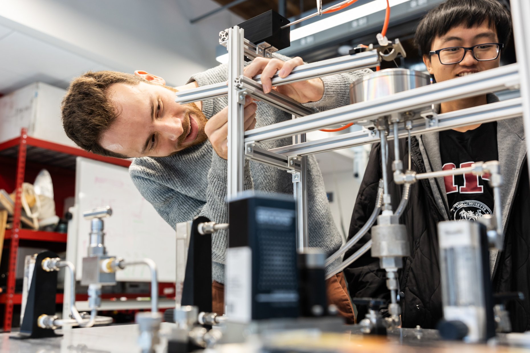 Two young men working on an engineering or robotics project with metal and plastic parts in a workshop or lab.
