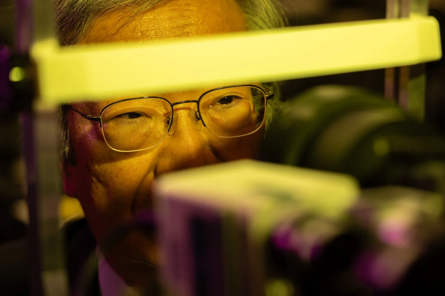Close-up of a woman wearing glasses, looking through a piece of equipment with yellow lighting.