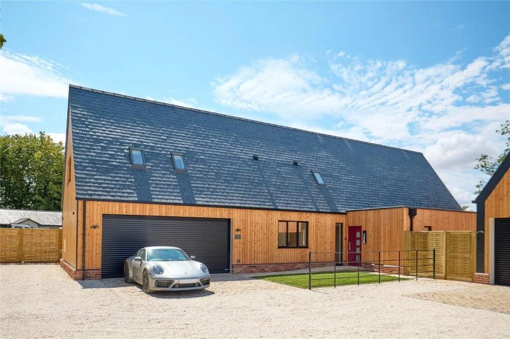 Modern timber-clad country home with a slate roof and gravel courtyard in a rural setting.