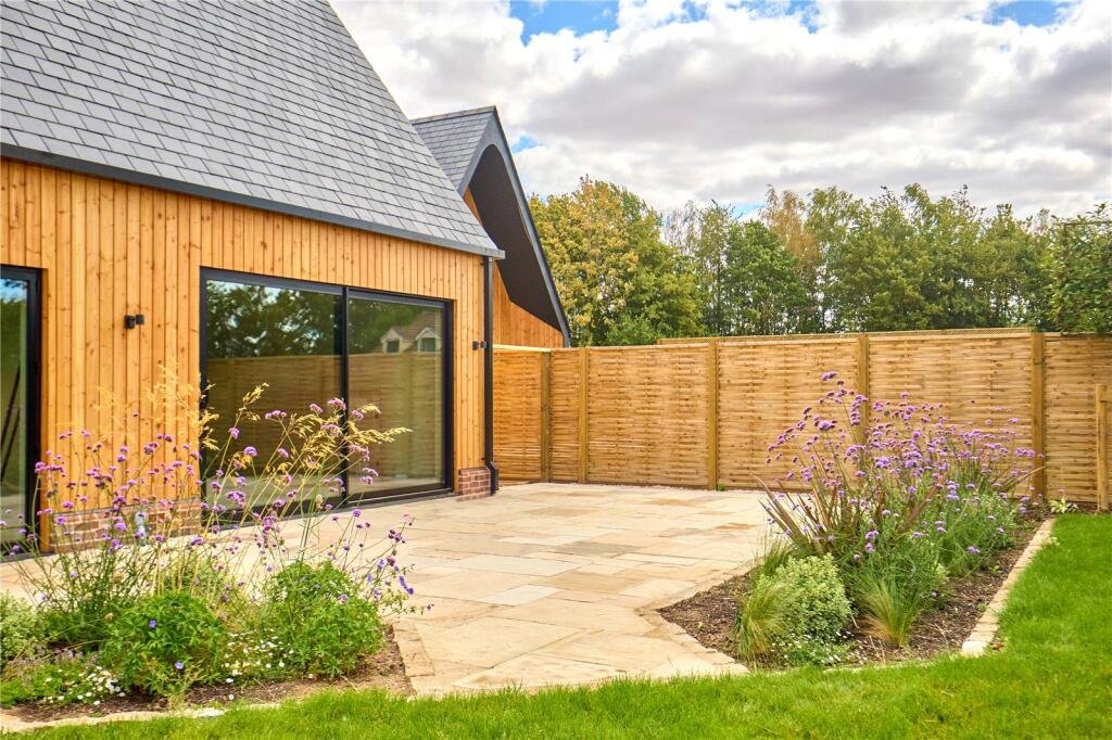 Modern timber-clad country home with large sliding doors, paved terrace and landscaped garden.