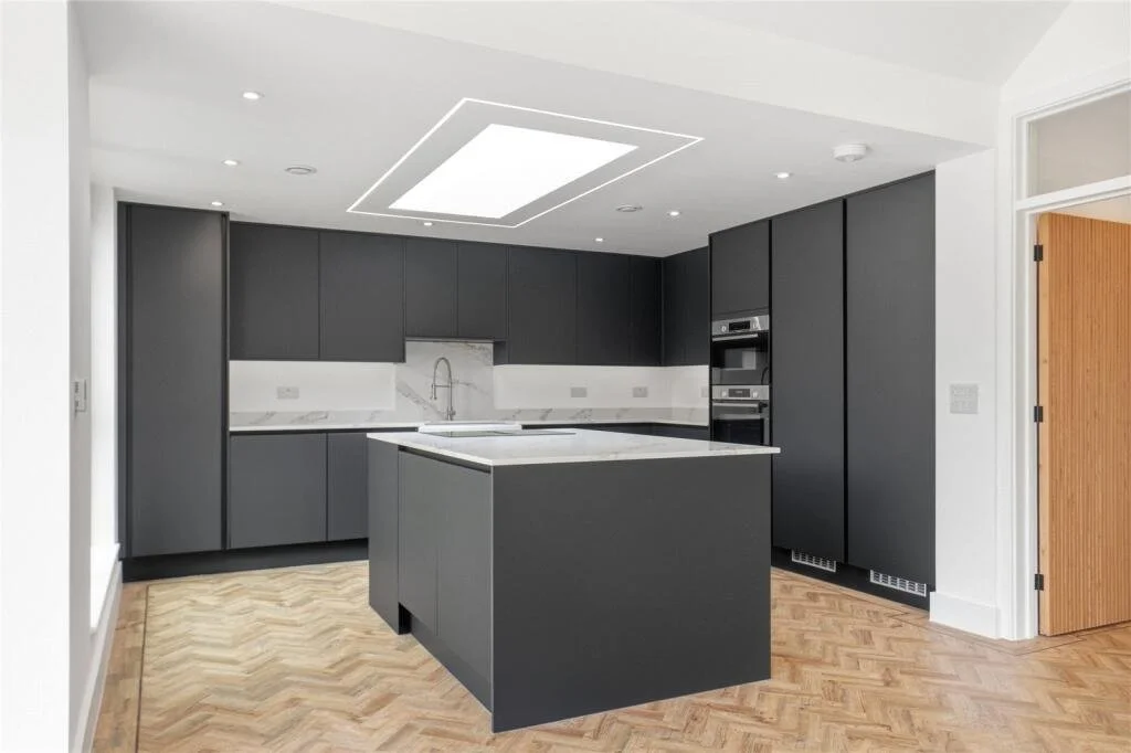 Modern charcoal kitchen with a central island, marble-effect worktops, skylight and herringbone wood flooring.