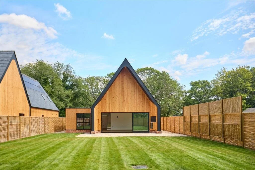 Contemporary timber-clad home with a steep pitched roof, large sliding doors and a landscaped lawn.