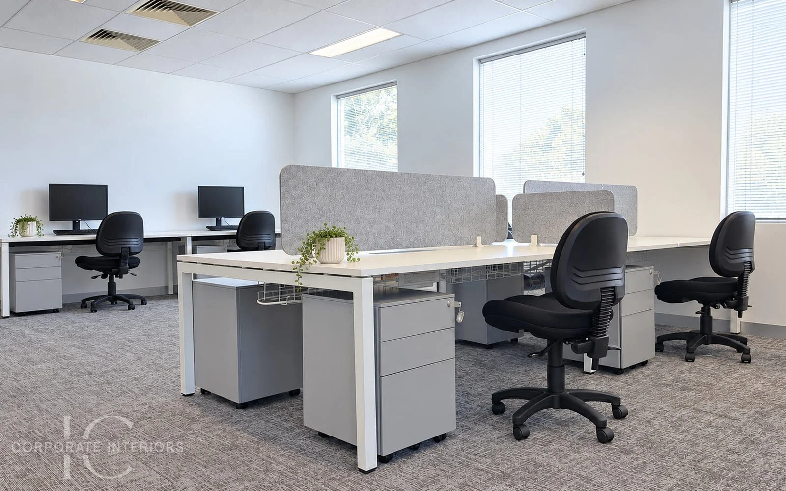 Open plan office workstations with grey acoustic divider screens, black ergonomic office chairs, mobile pedestals and computer monitors.
