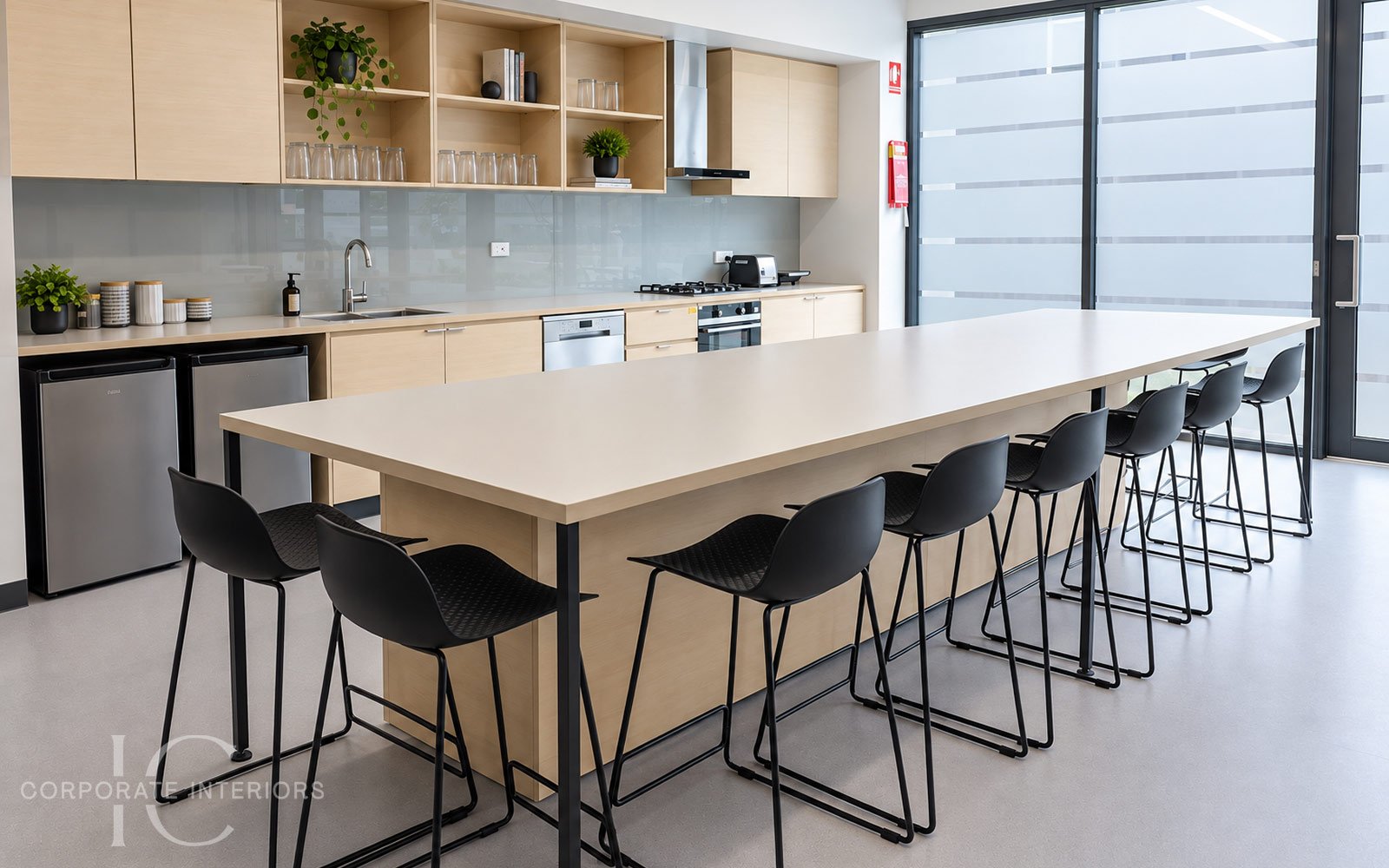 Staff kitchenette with black counter stools, large breakout table and coordinated timber cabinetry.