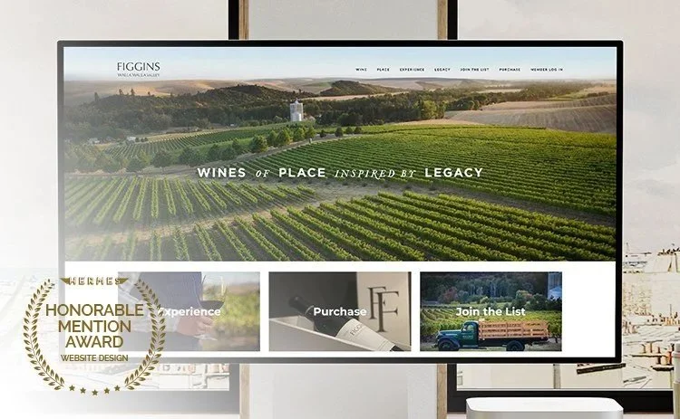 Computer monitor displaying a vineyard website with navigation menu, images of wine, purchase options, and a nature scene background, alongside an award badge for website design.
