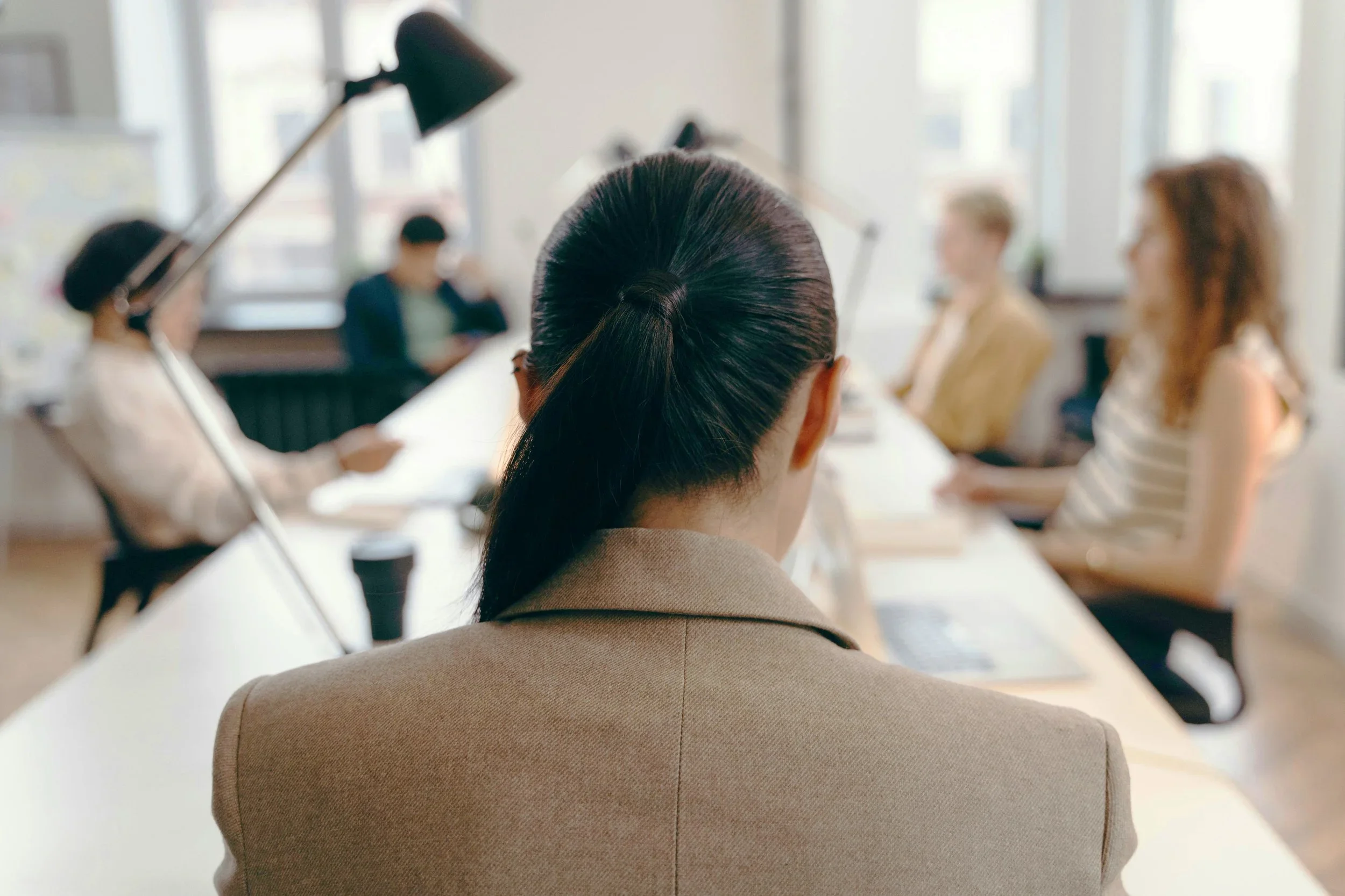 back of woman's head at long table at a meeting with other people