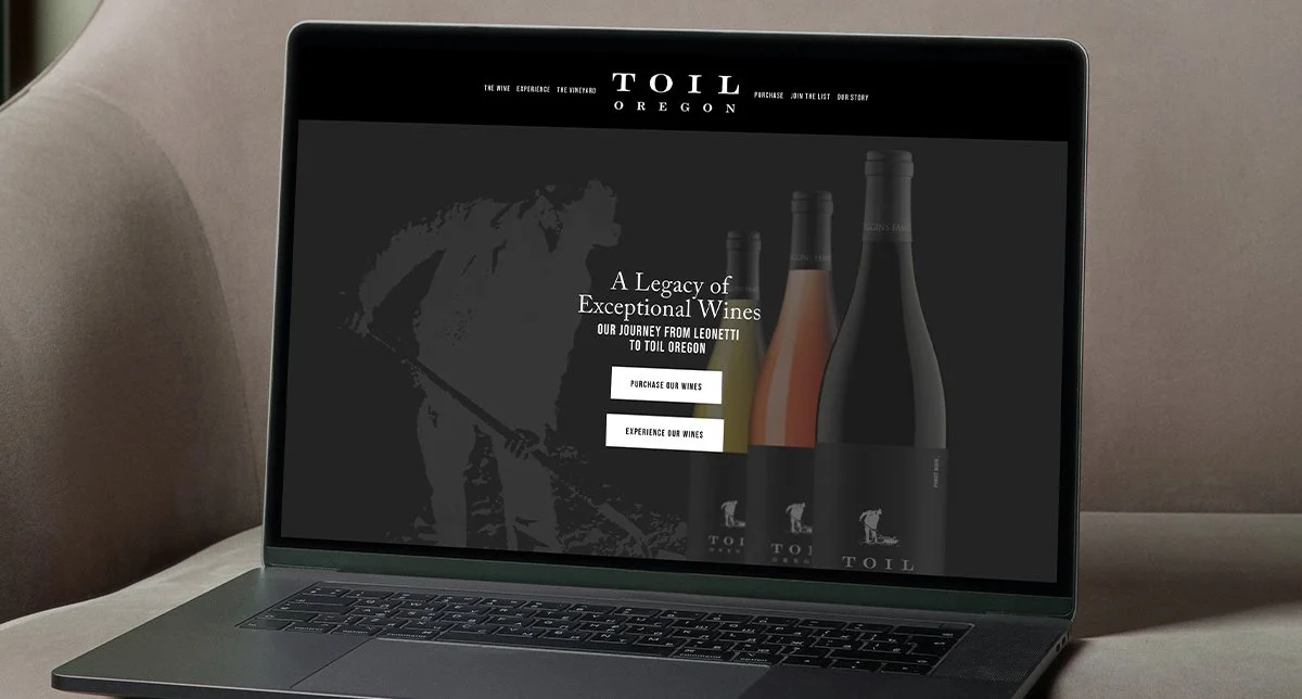 Laptop displaying a website for TOIL Oregon winery with bottles of wine and a graphic of a person working in a vineyard.
