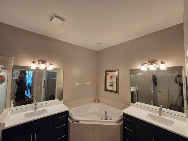 Bathroom with two sinks, large mirrors, a corner bathtub, and wall-mounted light fixtures.
