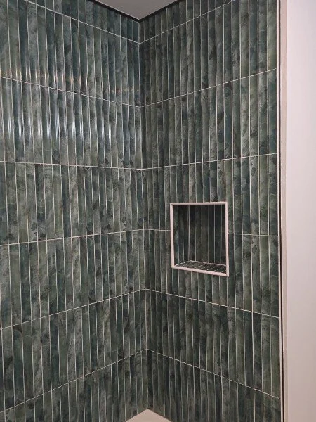 Green tiled shower wall with a built-in recessed shelf.