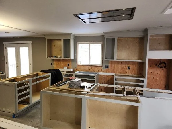 Kitchen under renovation with new cabinets being installed, no countertops yet, and tools on the countertops.