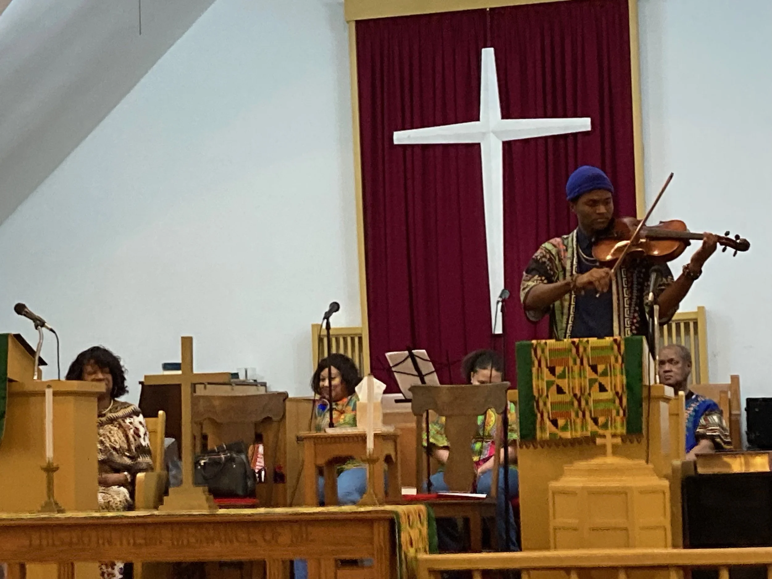 a man playing violin in front of a banner with a white cross