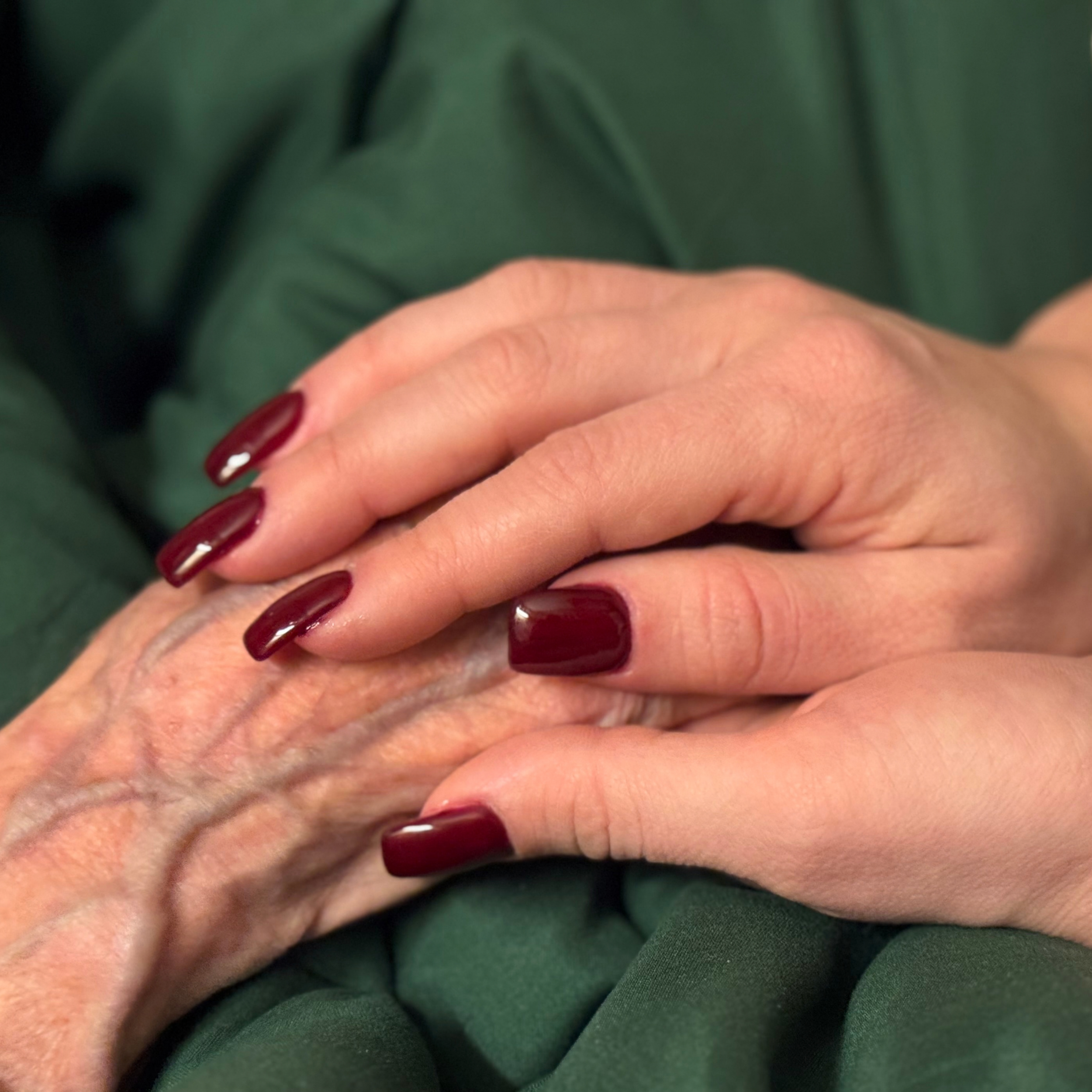 Youthful hands with painted nails holding senior hand.