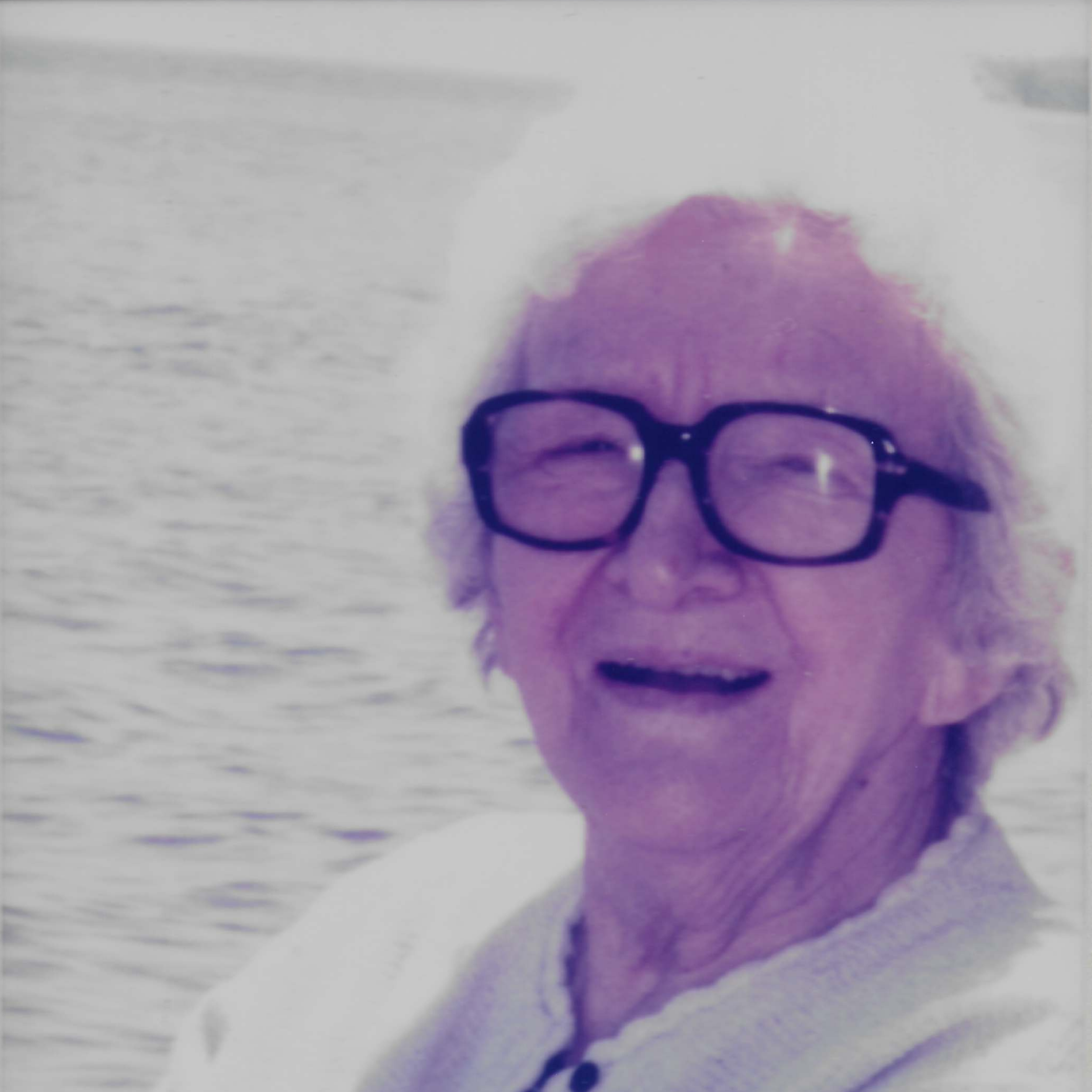 Old phWoman with glasses smiling in front of Lake Superior in the Upper Peninsula of Michigan.
