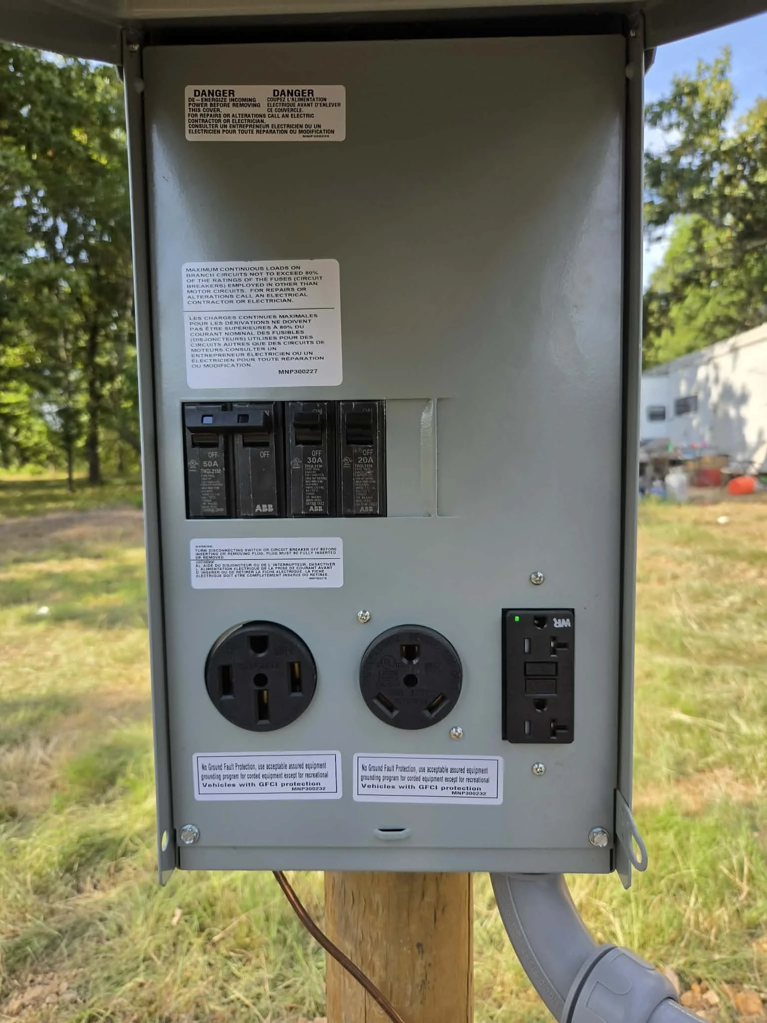 An outdoor electrical box mounted on a wooden post with circuit breakers, electrical outlets, and warning labels.