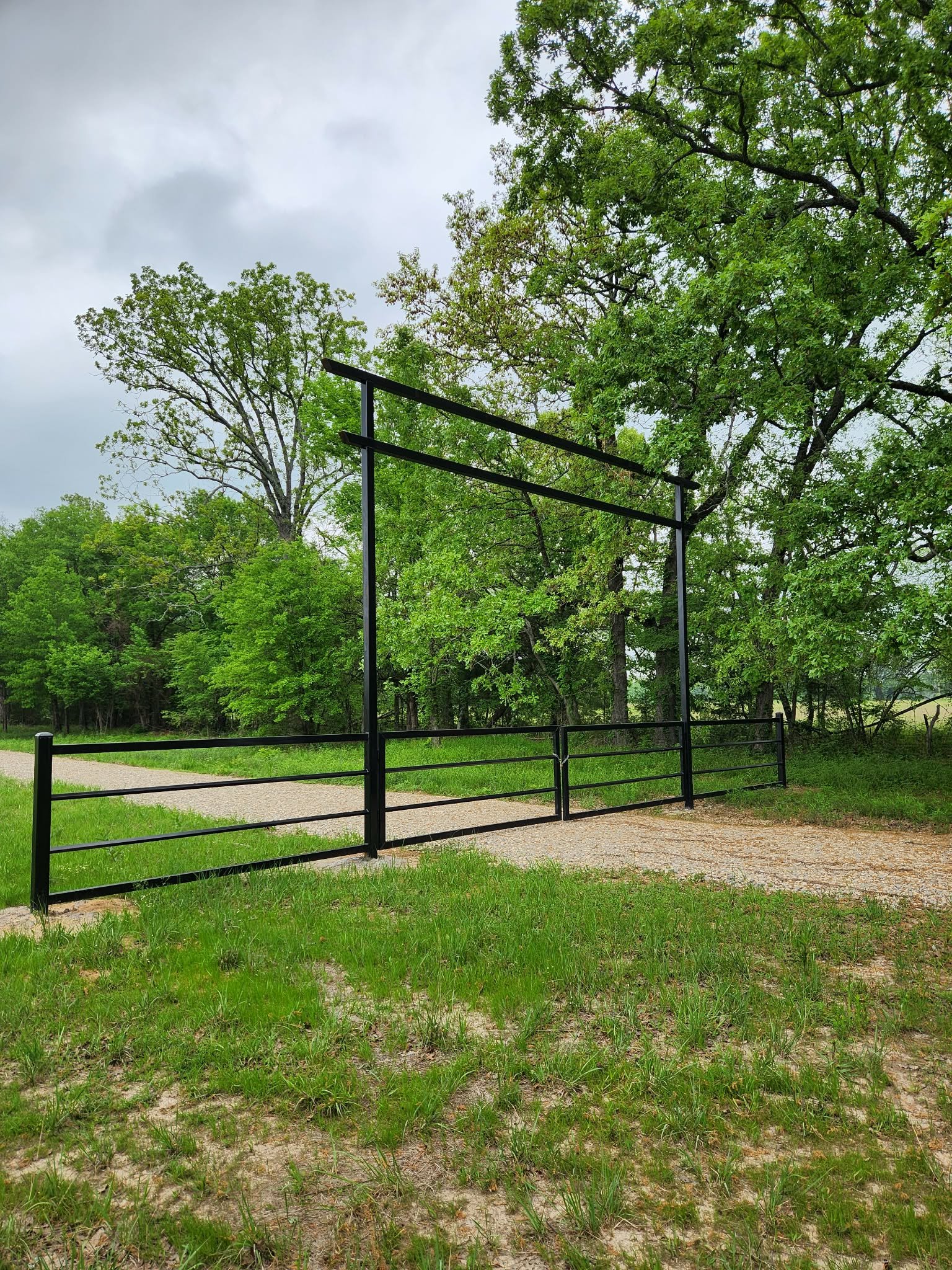 Metal structure with two horizontal bars in a lush green park with trees and a gravel path.