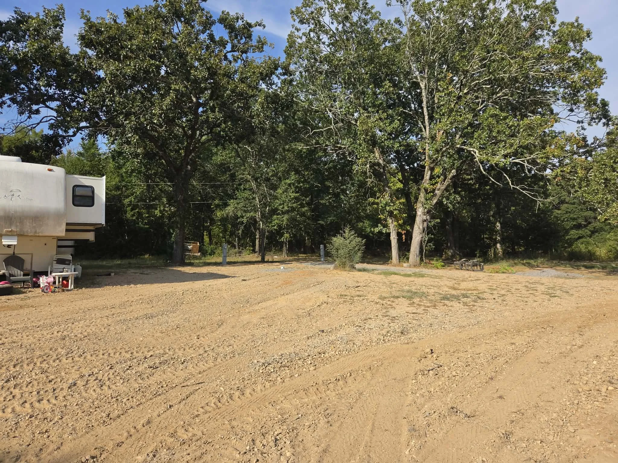 A dirt cleared patch of ground with trees in the background and part of a camper or trailer on the left side of the image.