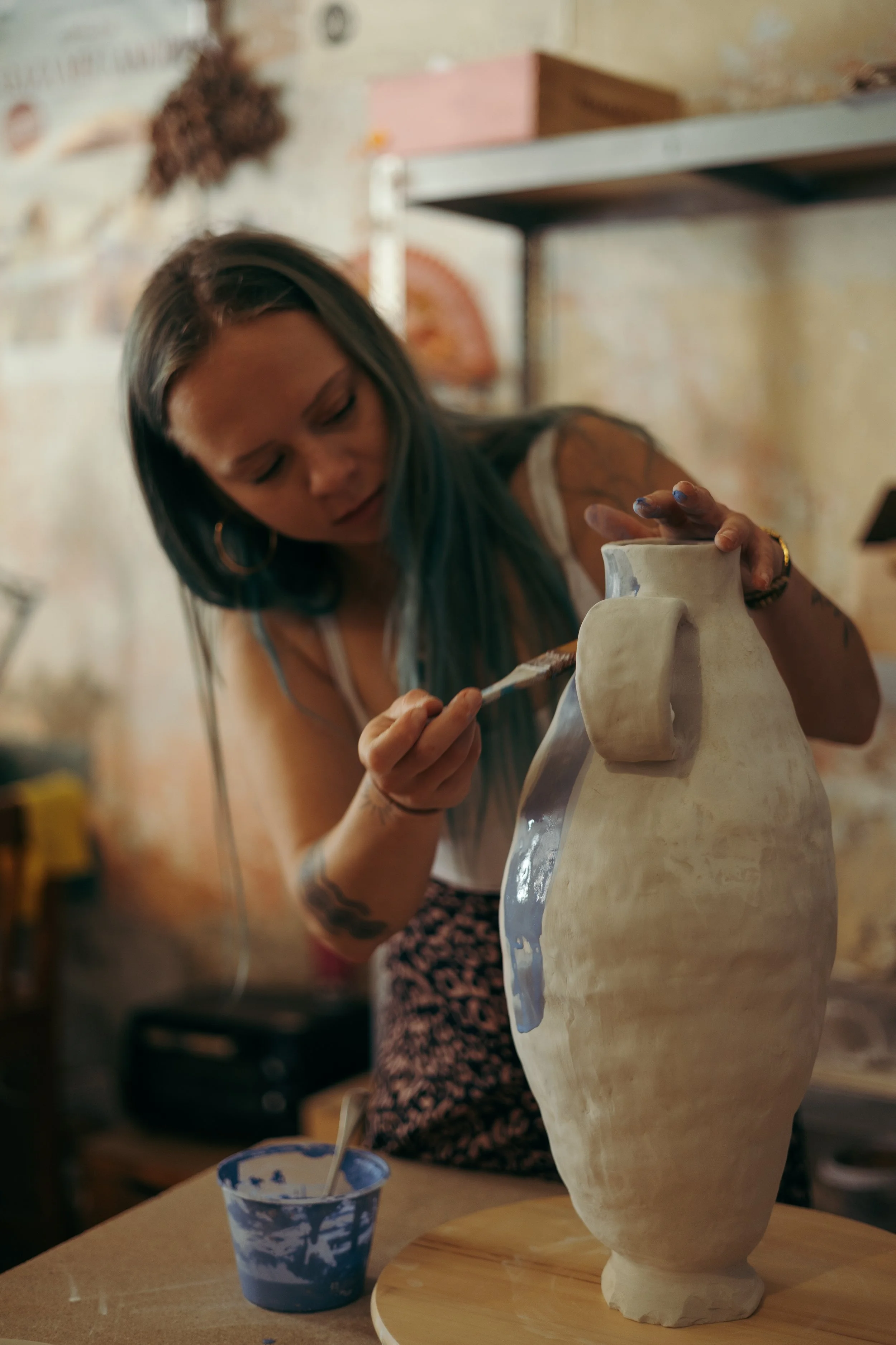 A woman painting a ceramic vase with a brush in a pottery studio.