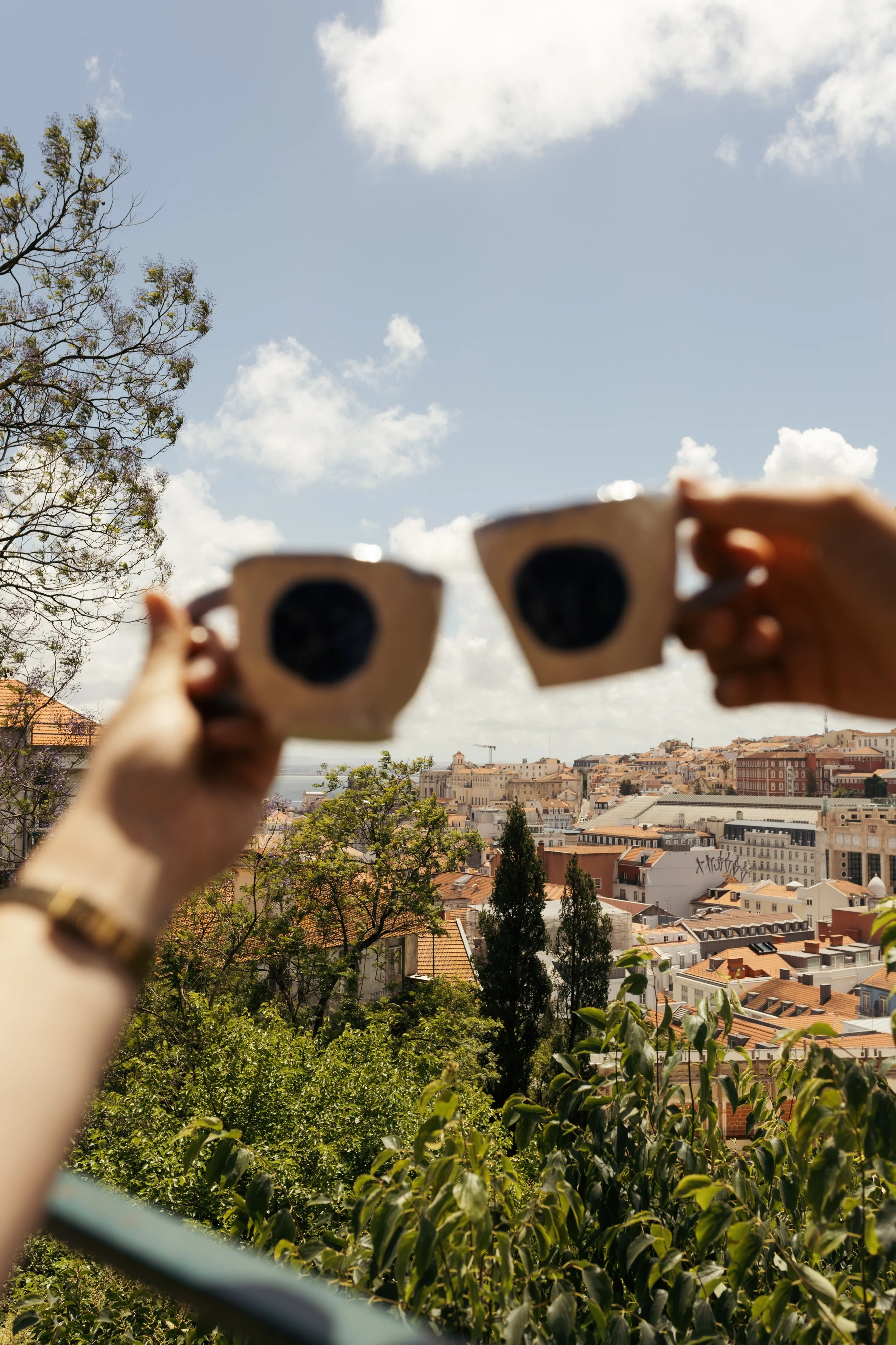 People holding coffee mugs in front of a cityscape with rooftops, trees, and buildings under a partly cloudy sky