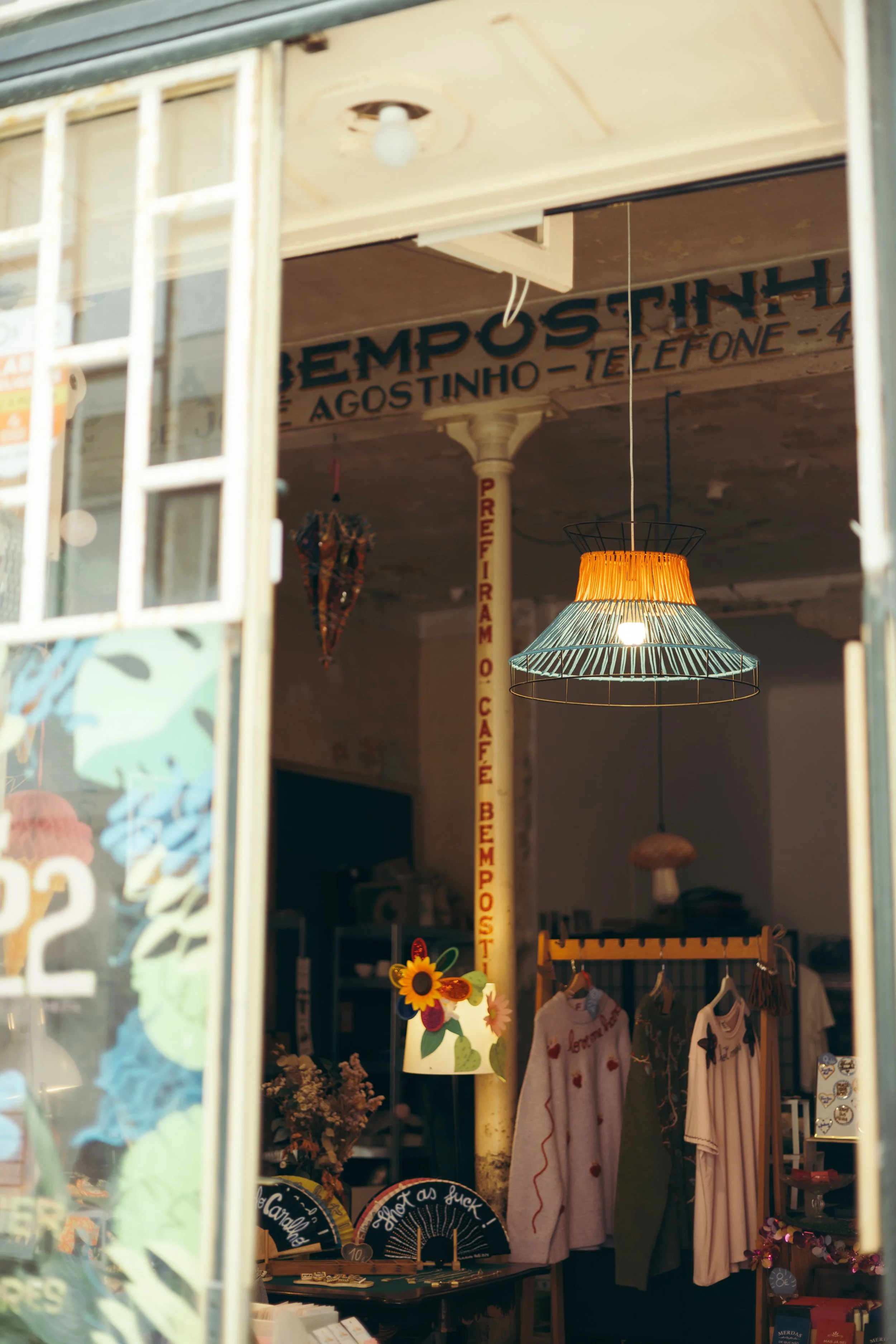 View of a boutique shop interior with hanging light fixtures and clothes on display, visible through a shop window.