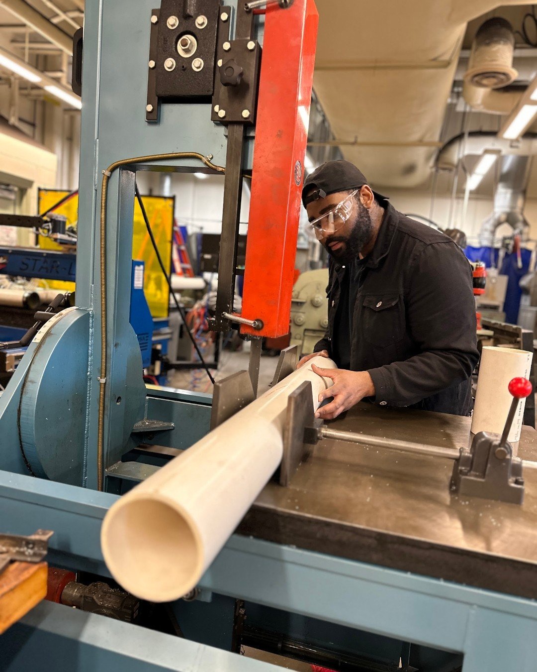 Wes Banks machining components for an aeroponics tower with a rolling bandsaw in a university machine shop