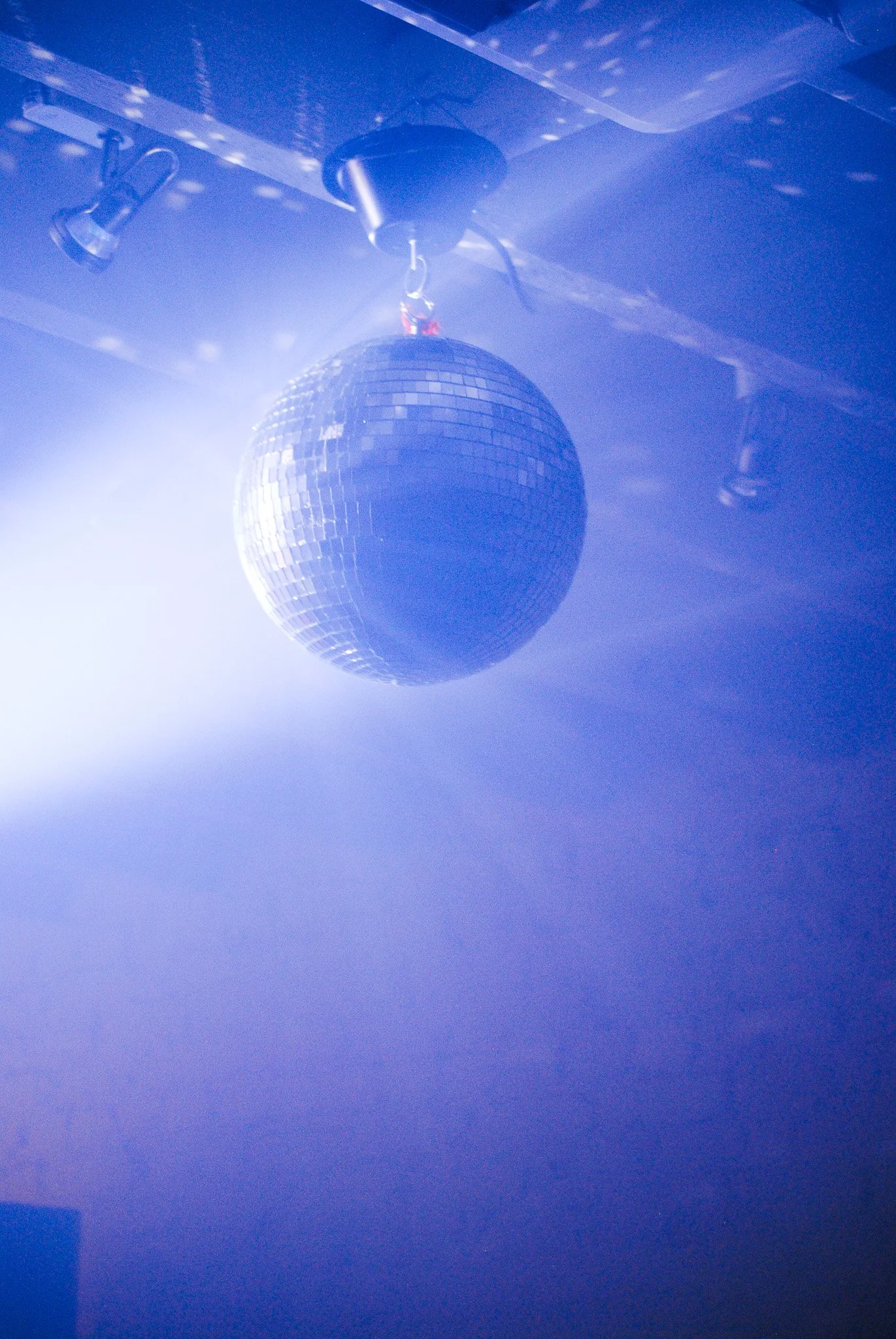 A disco ball hanging from a ceiling, reflecting light and creating a sparkling effect in a blue-lit room.