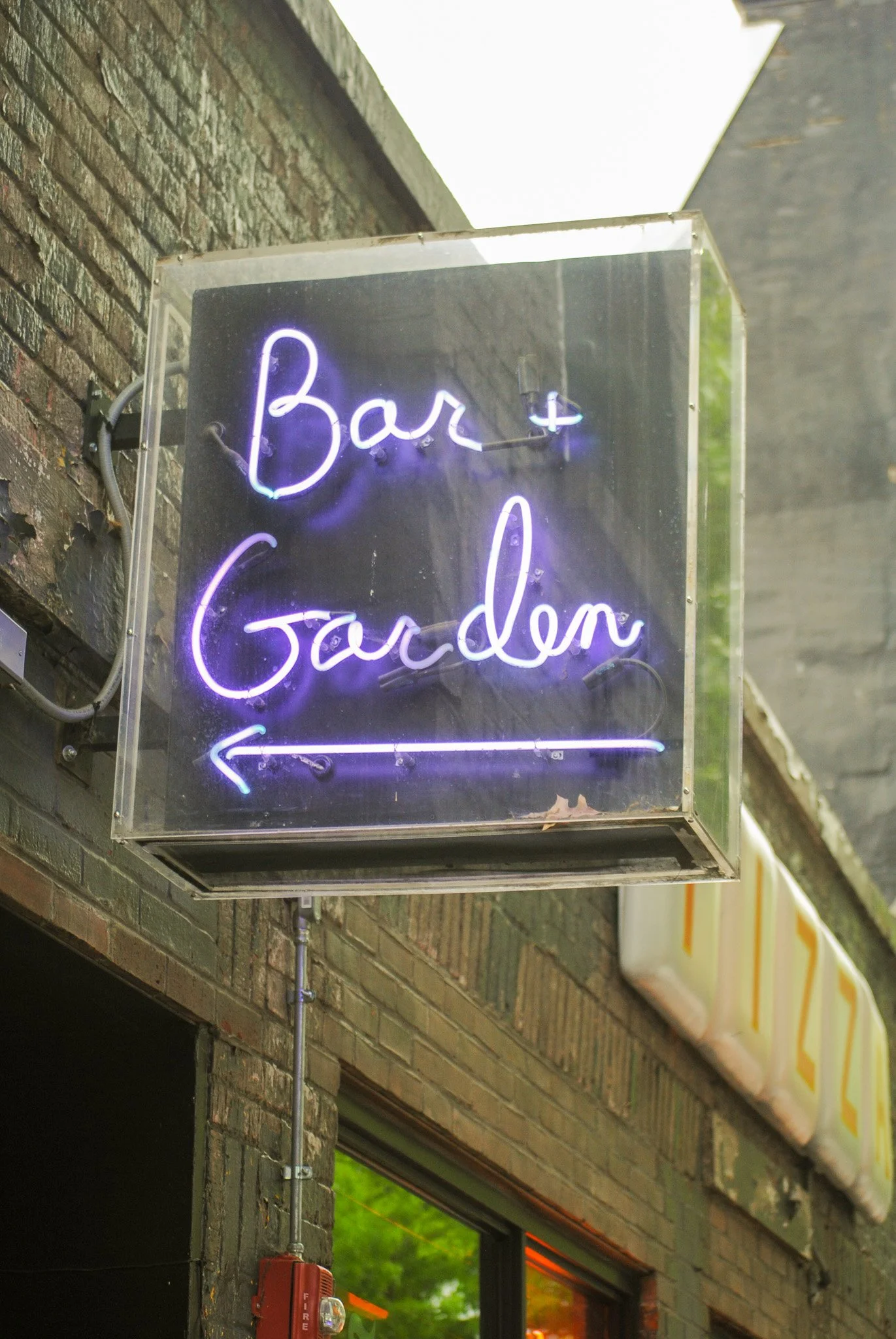 Neon sign reading 'Bar & Garden' with an arrow pointing left, mounted on a brick wall outside a building