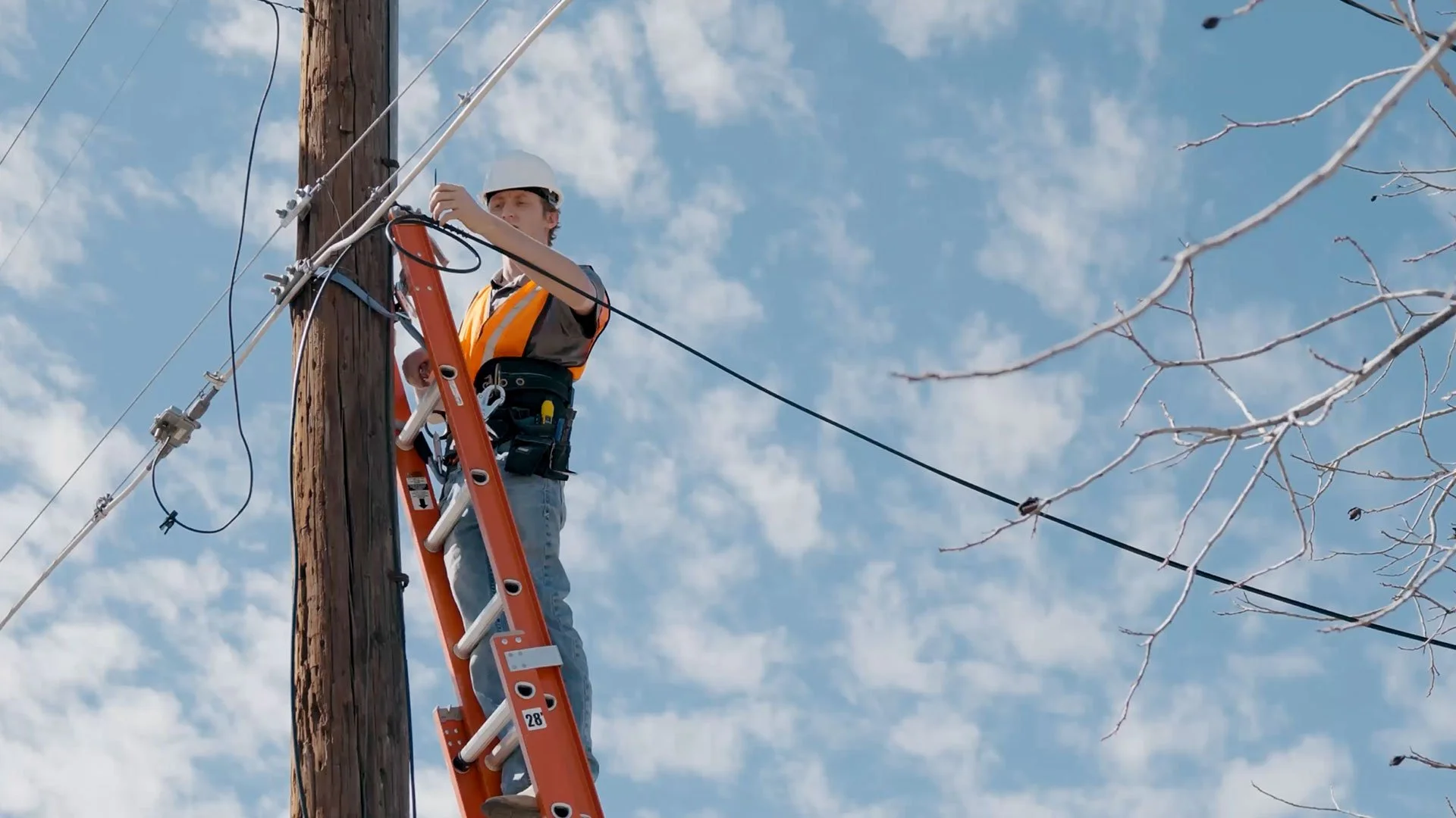 A telecommunications contractor installing a cable line on an aerial pole in Texas.