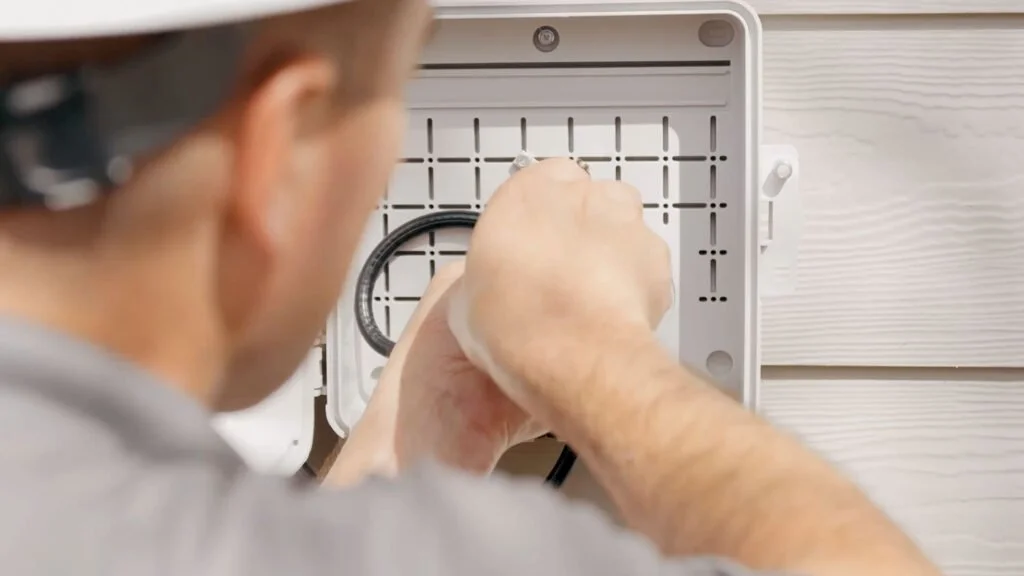 Technician working inside an open electrical box on a house exterior.