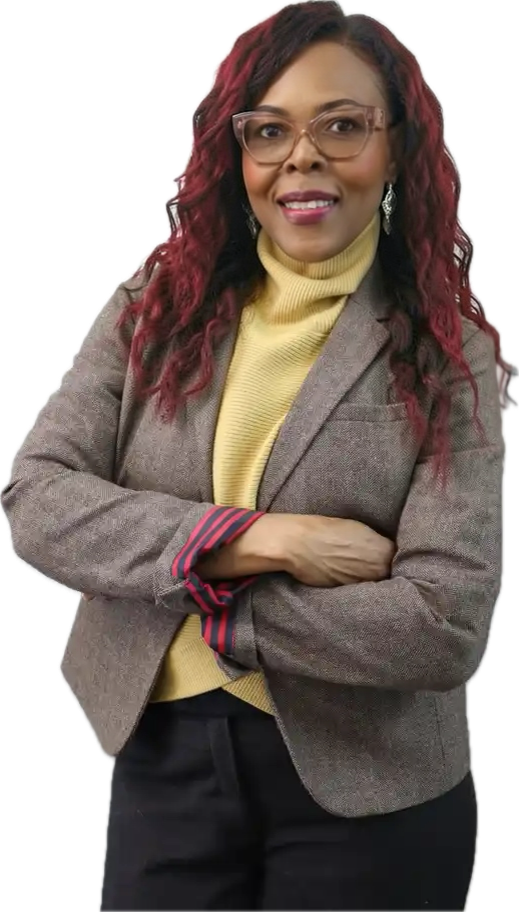 Woman in glasses with red curly hair wearing a gray blazer with rolled-up sleeves over a yellow turtleneck, smiling with arms crossed