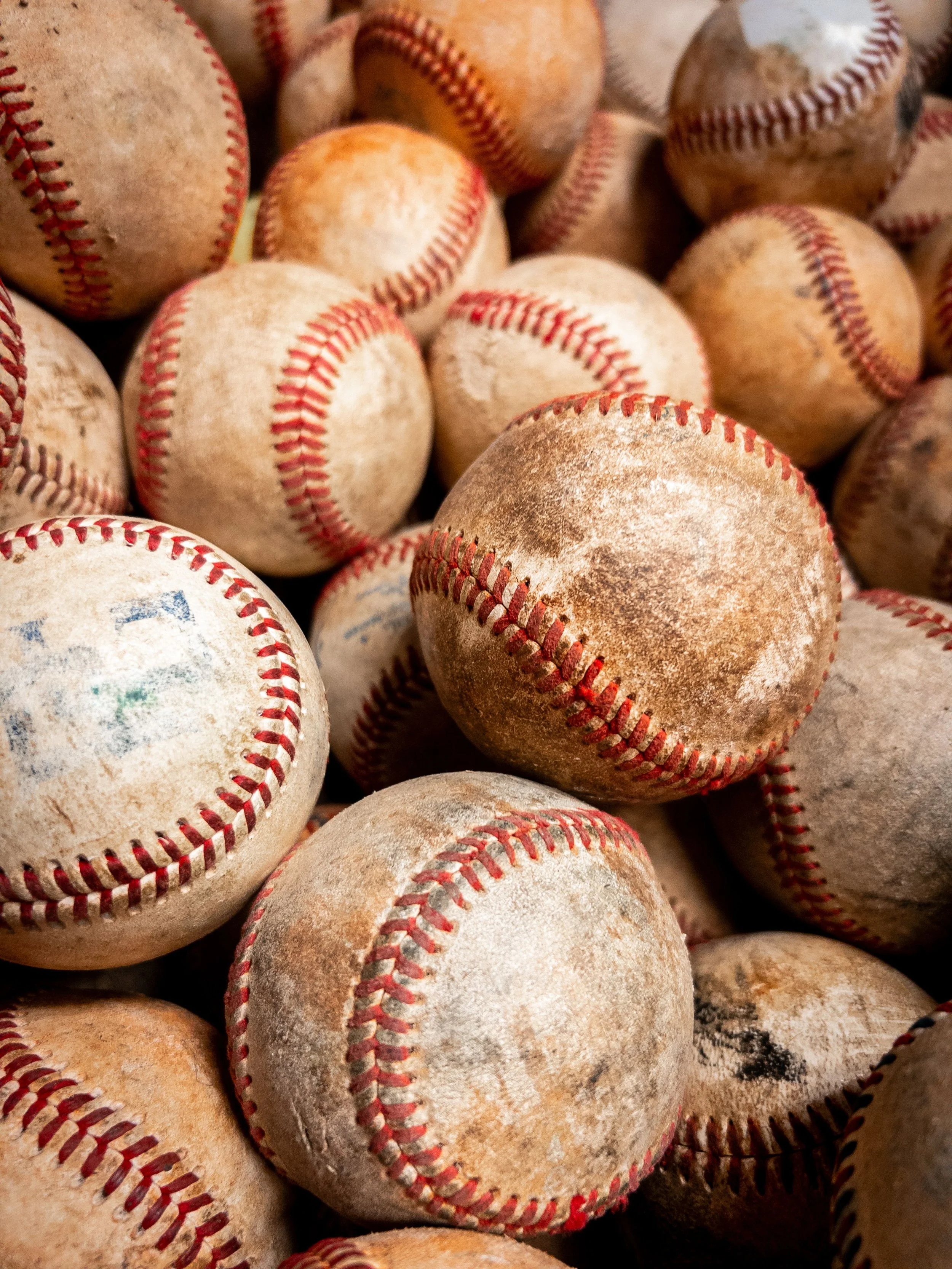 A close-up of numerous well-worn baseballs with visible dirt and faded stitches.