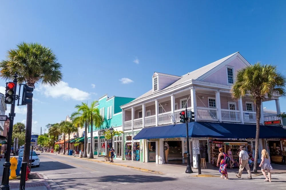 Colorful buildings on a sunny street with palm trees and pedestrians.