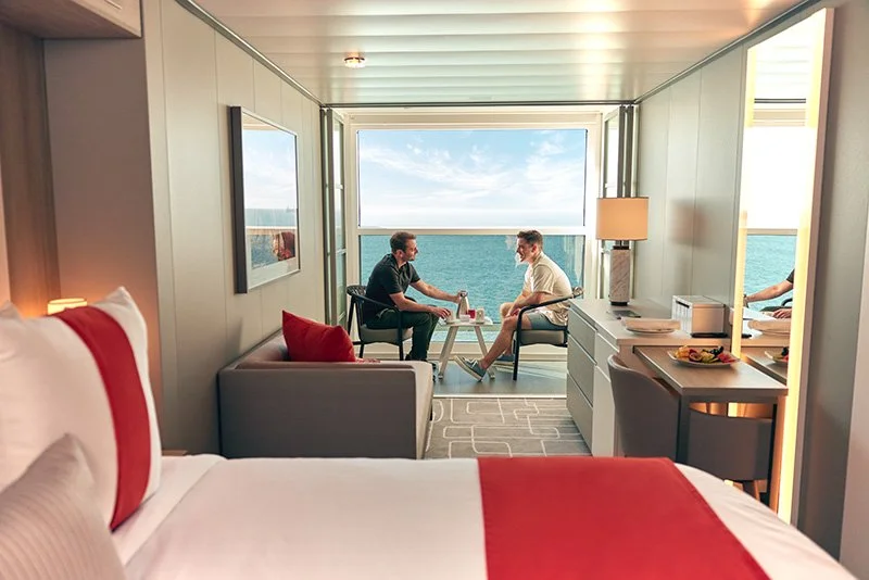 Two men are sitting and talking on a balcony overlooking the ocean.