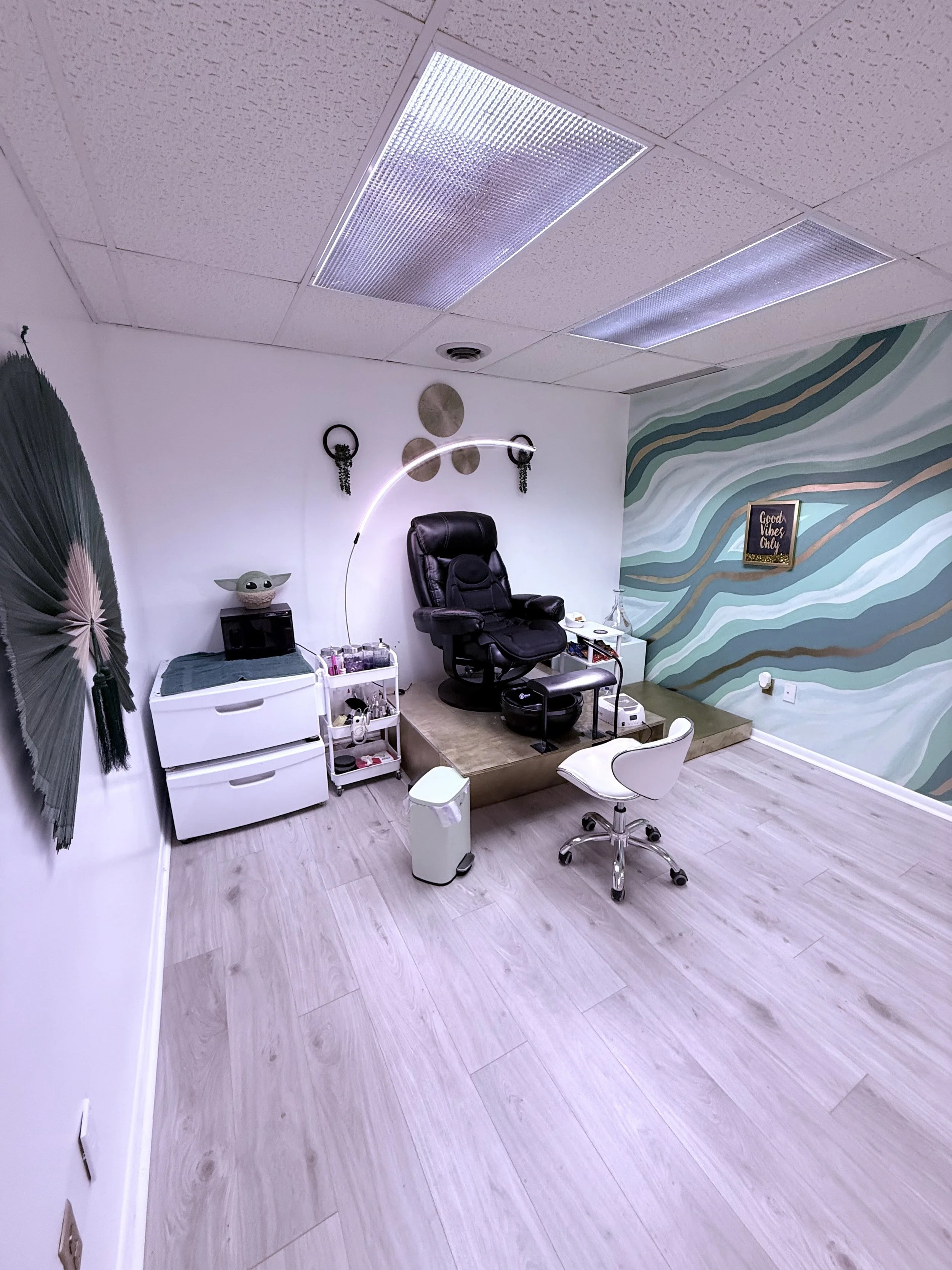 A cozy room with a black massage chair, decorative wall art, and a sign that says 'Good Vibes Only'.