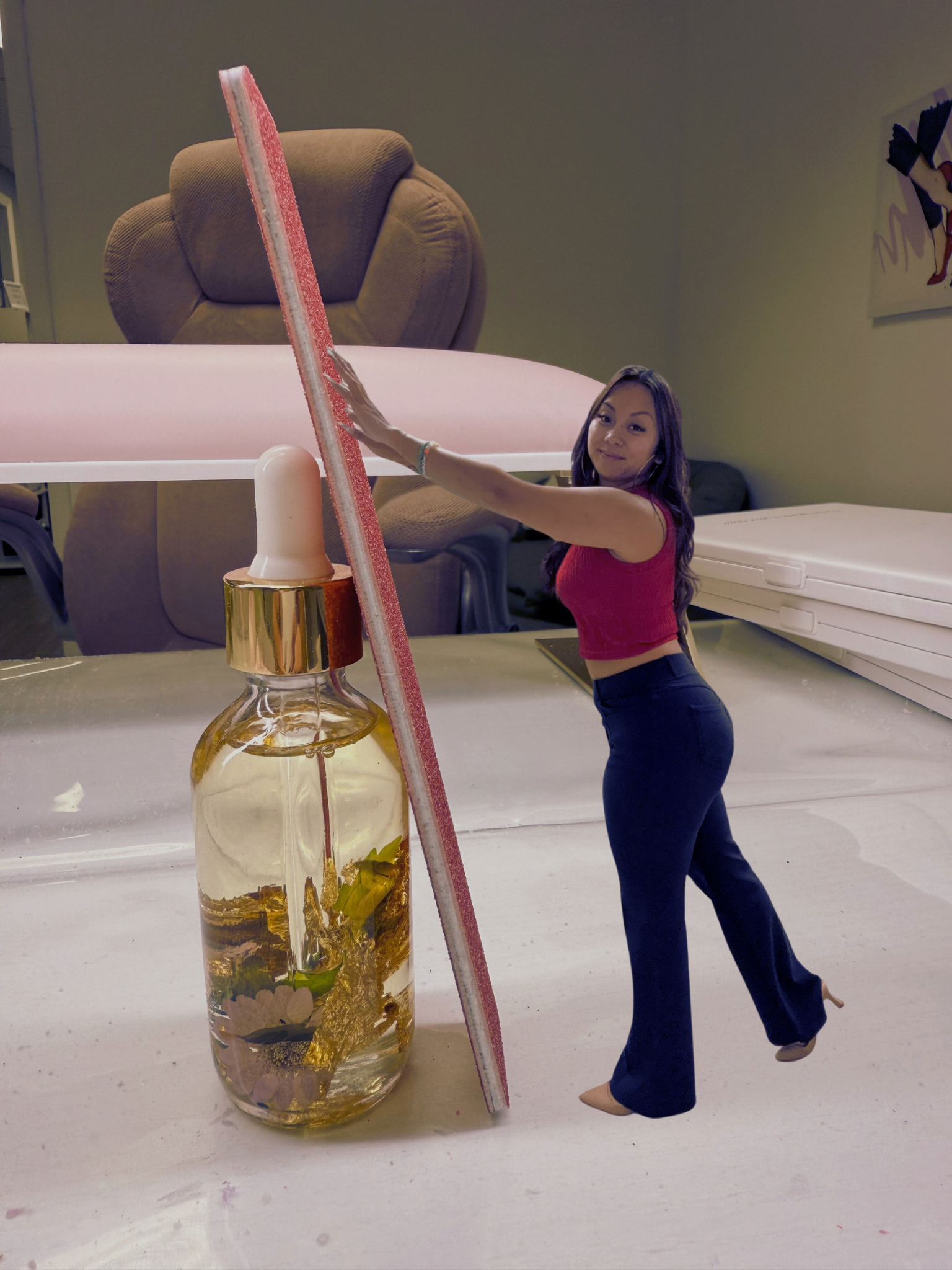 A woman with long dark hair, wearing a red sleeveless top and navy pants, is standing next to a large glass bottle with yellow flowers inside. She is reaching out with her right hand to touch a long pink and white object that leans against the bottle. The background includes a beige armchair and a wall with a piece of artwork.