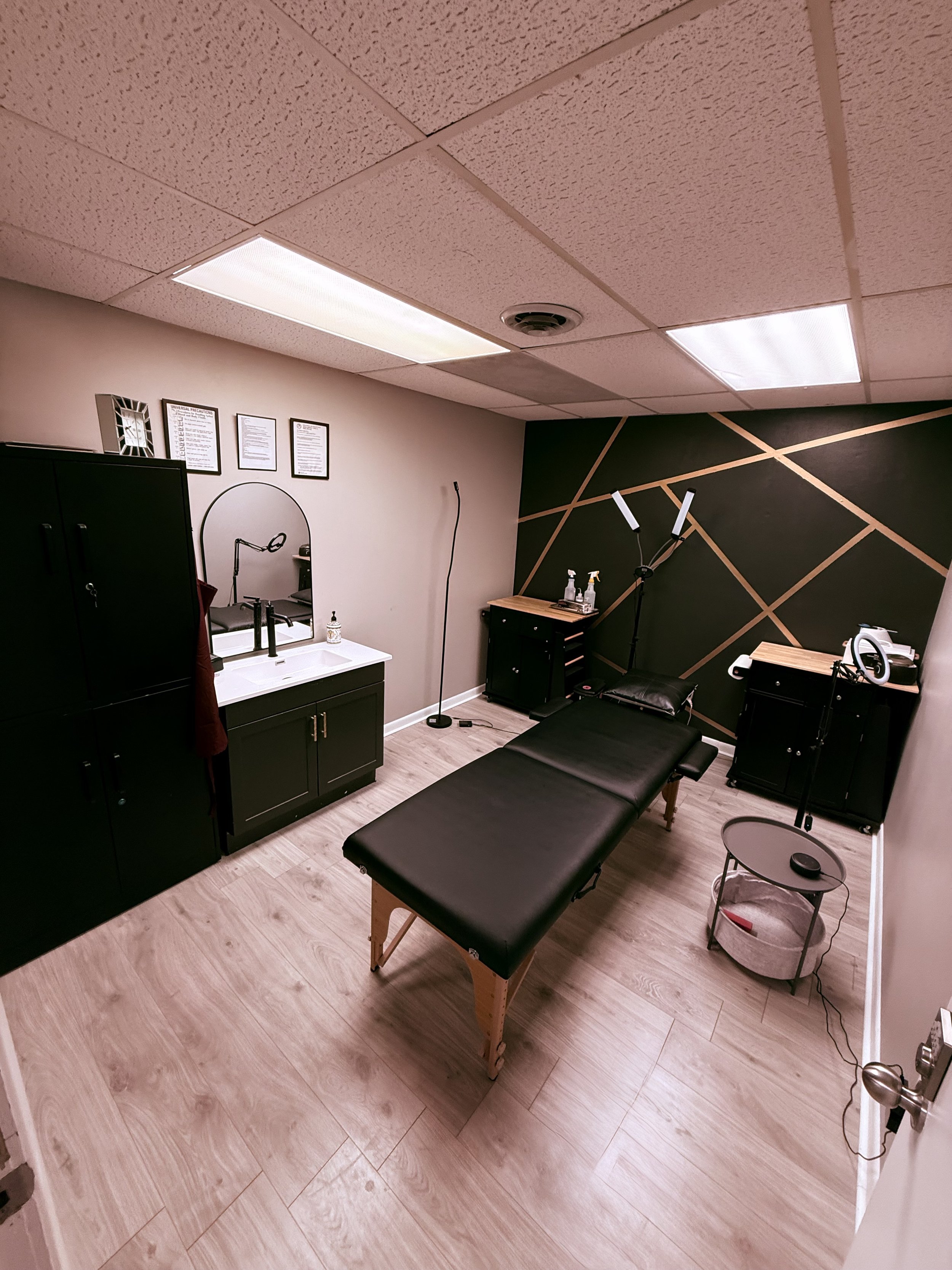 Medical examination room with a treatment table, black cabinets, a mirror, lighting, and medical equipment.