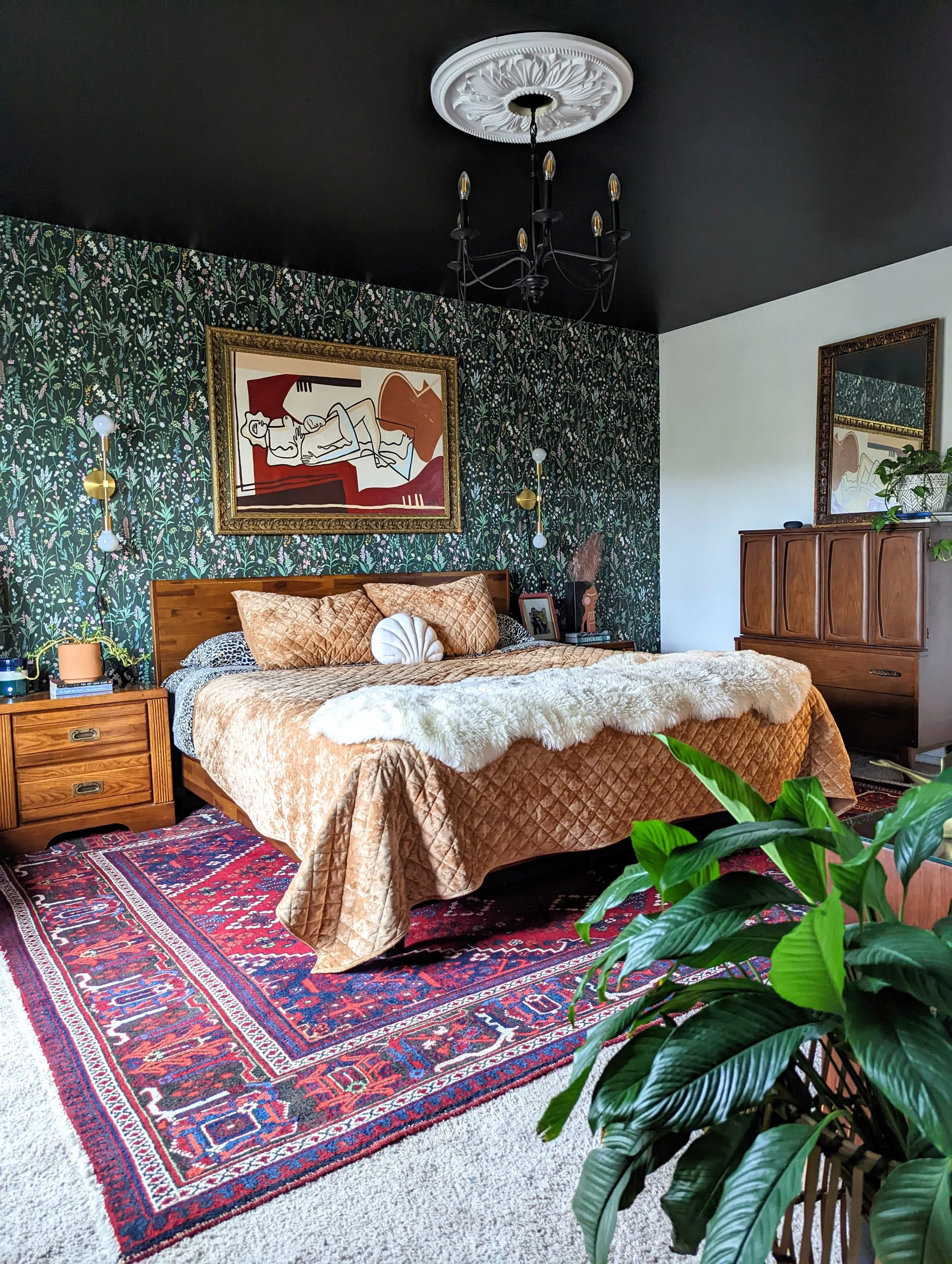 Moody bedroom in an Austin-area home featuring vintage furnishings, layered textiles, eclectic artwork, and a dark ceiling.